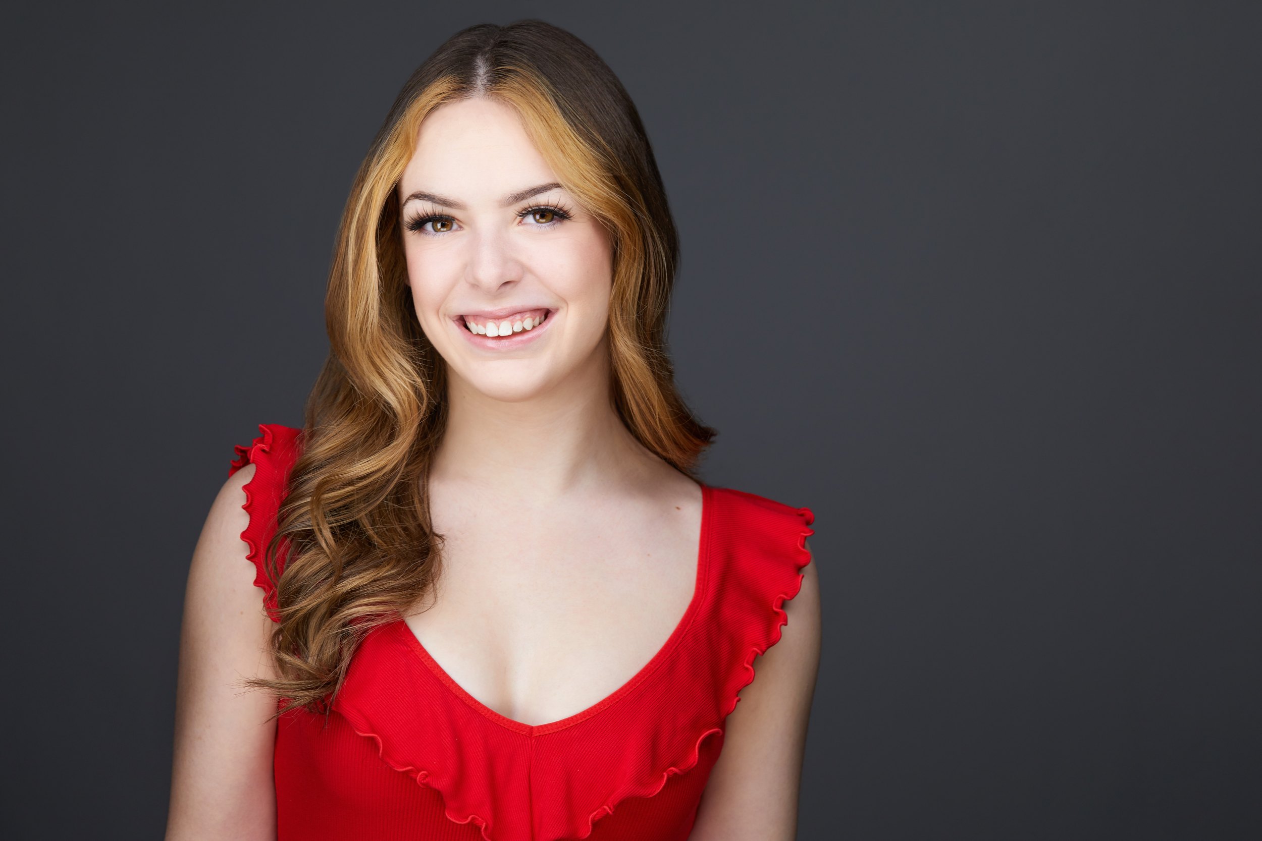 Dance headshot: a red ruffled top against grey, smiling
