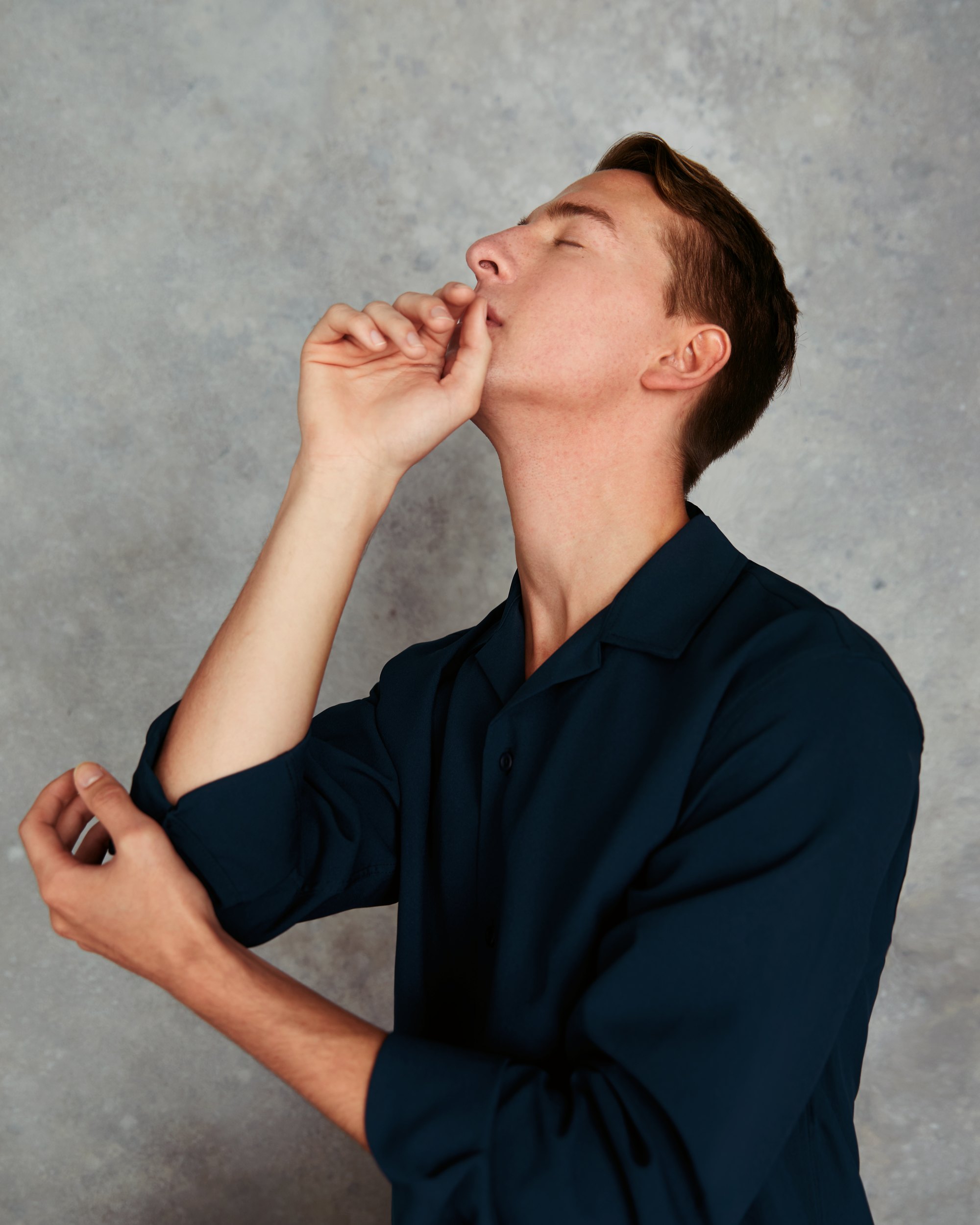 The same dancer in a navy shirt against grey, hands to his face, eyes closed