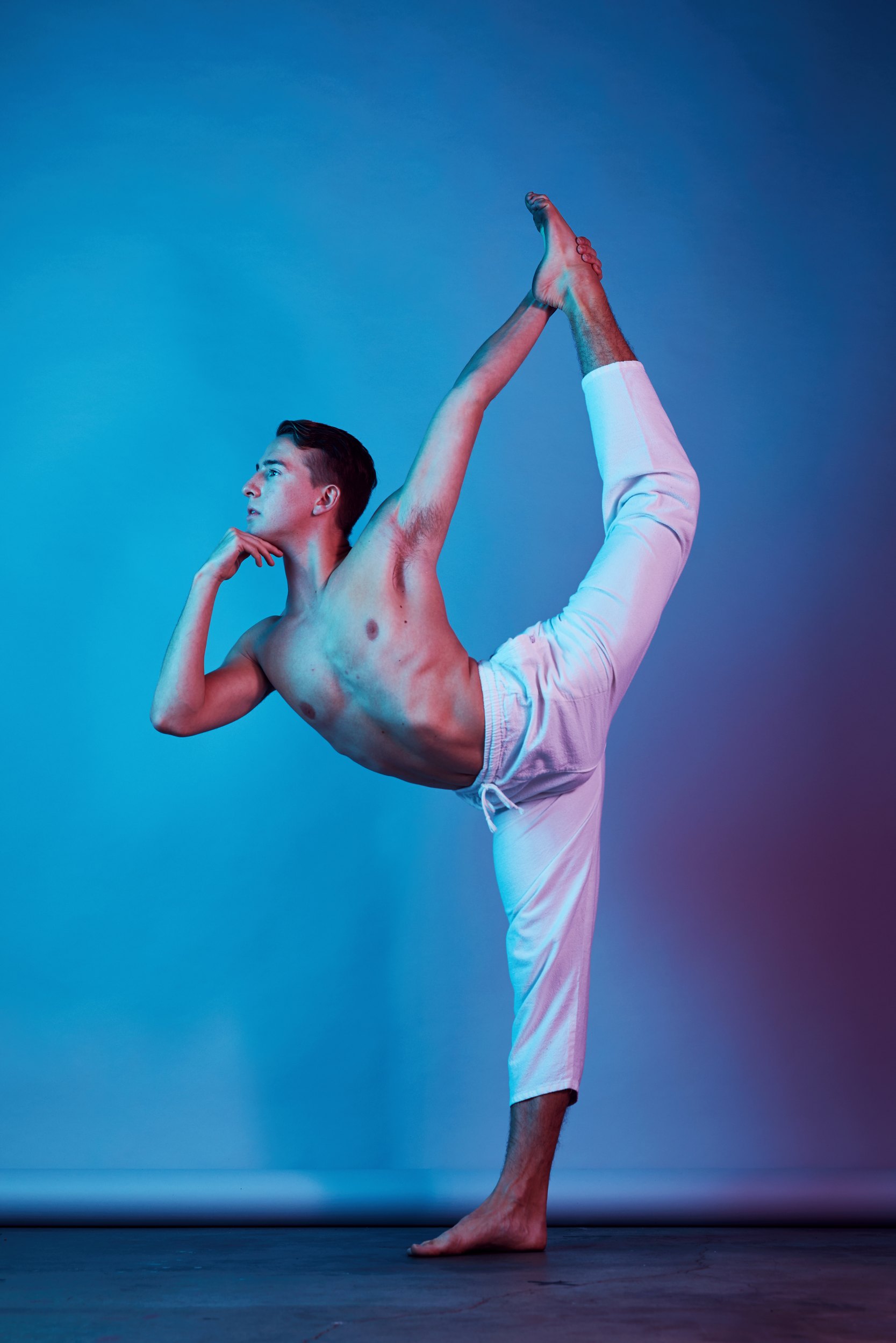 Under blue and pink gels: in white pants on one leg, the other foot pulled up behind him, chin on his hand