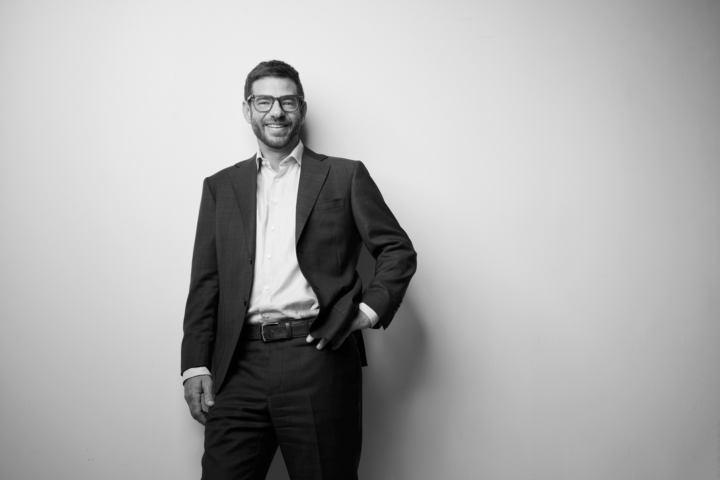 A portrait for BOMA, black and white: a man in a dark jacket and glasses, standing against white, full length