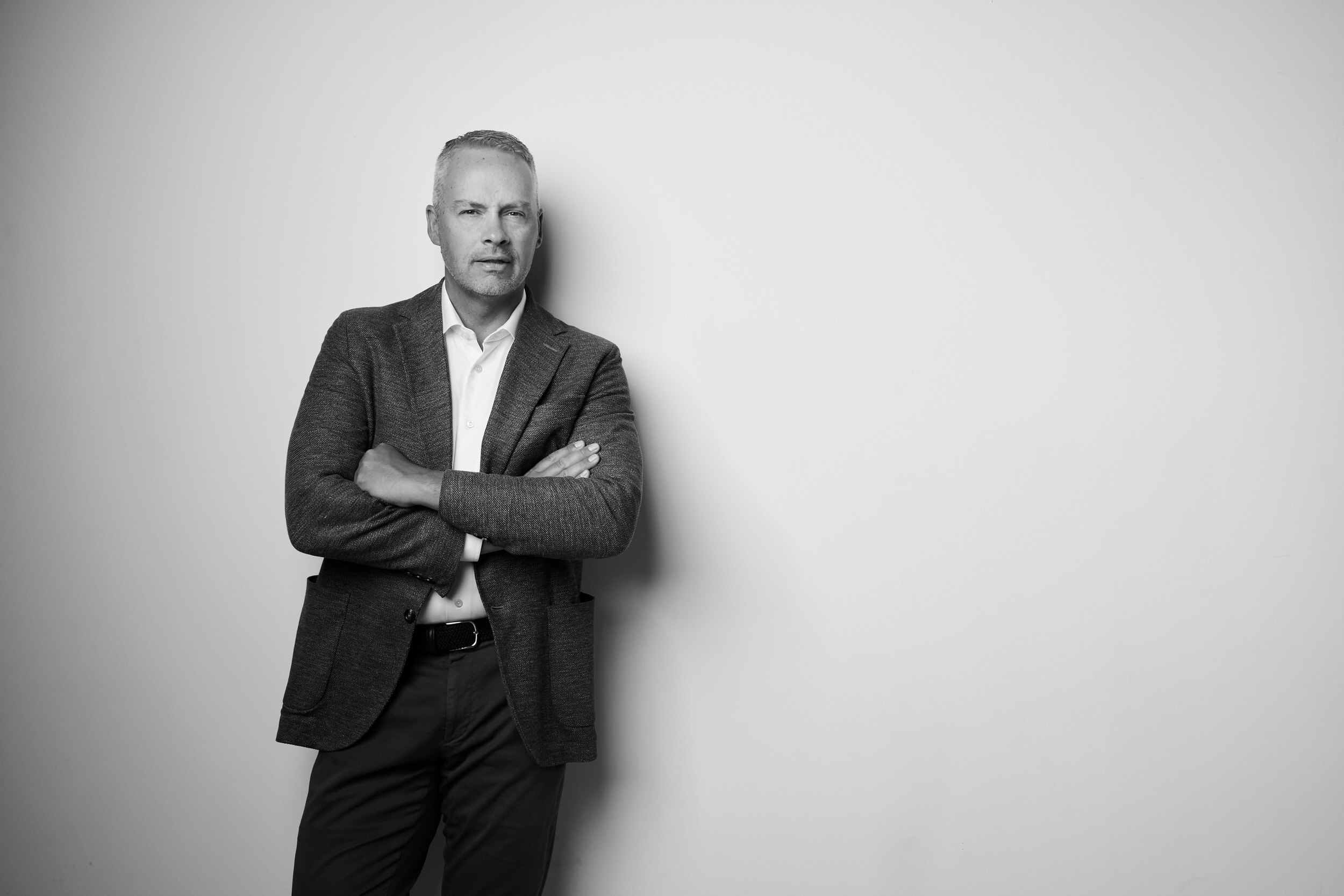 A portrait for BOMA, black and white: a man in a grey jacket, arms folded, against white