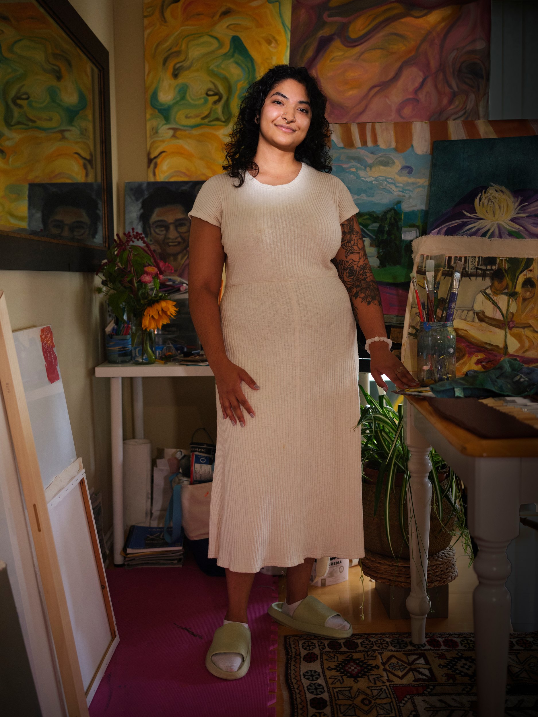 Kira Chankasingh in a cream dress, standing among her paintings
