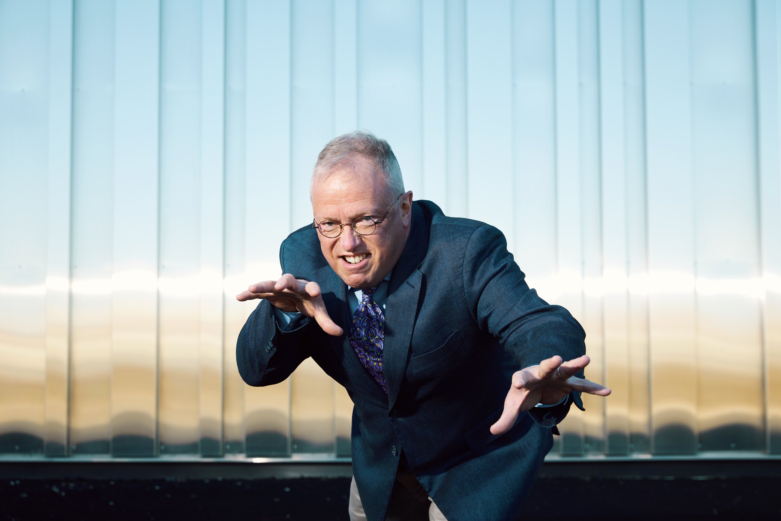 The same man leaning into the lens, hands out, mid sentence