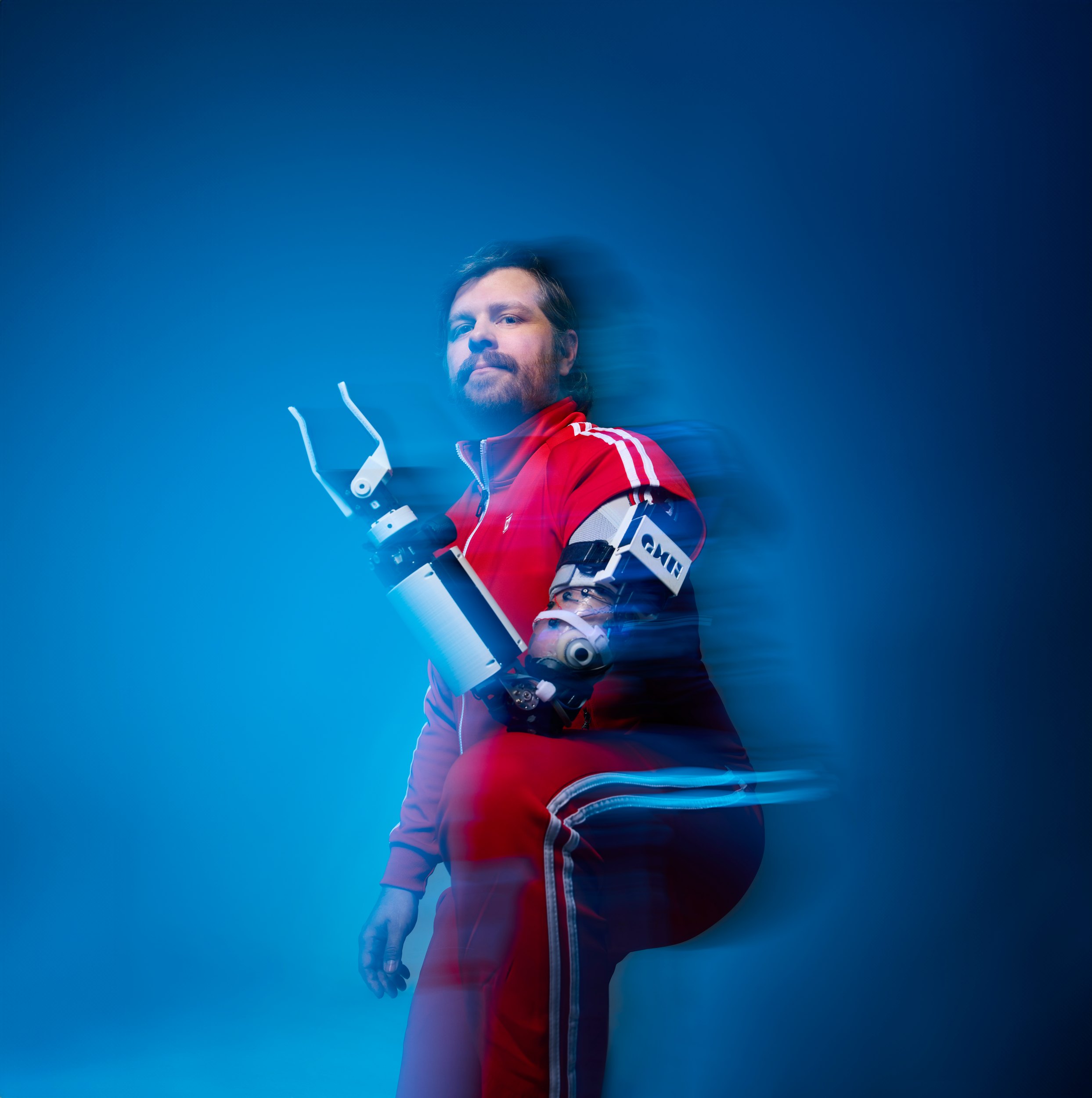The cover frame: leaning back in a red tracksuit, the bionic arm raised, the movement trailing behind him