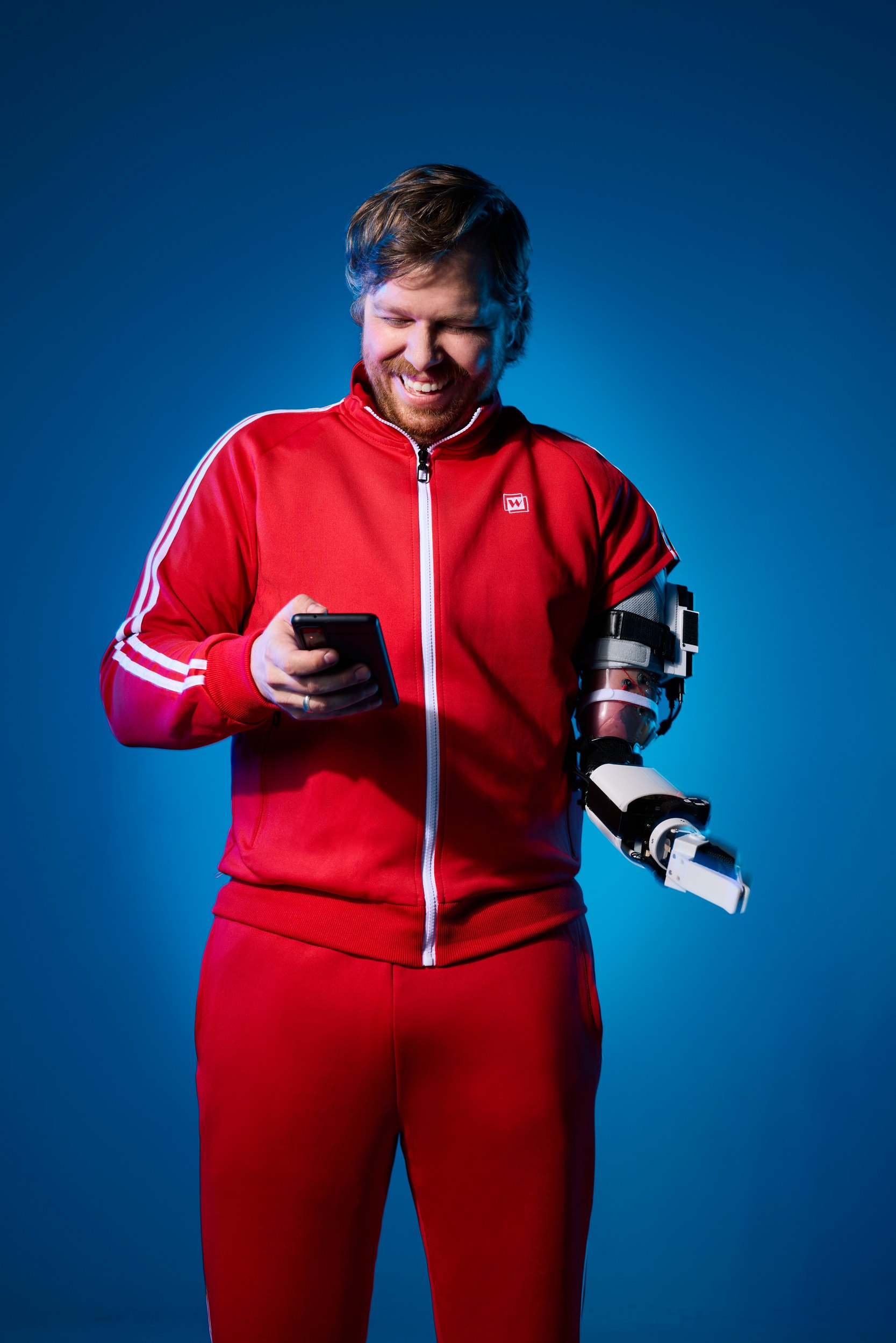 Standing on blue, looking down at a phone held in the prosthetic hand