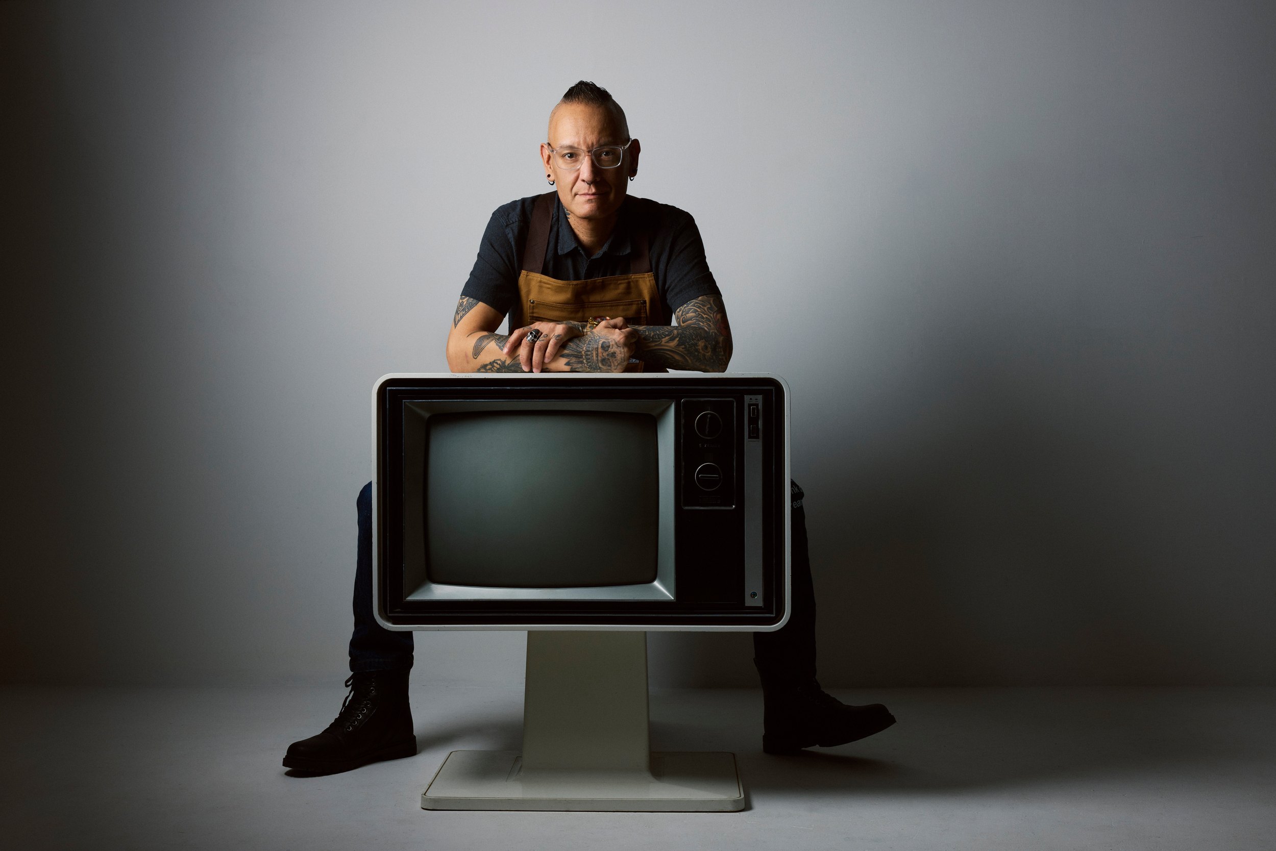 The frame the spread ran: the chef behind the television, arms folded, his initials on the screen