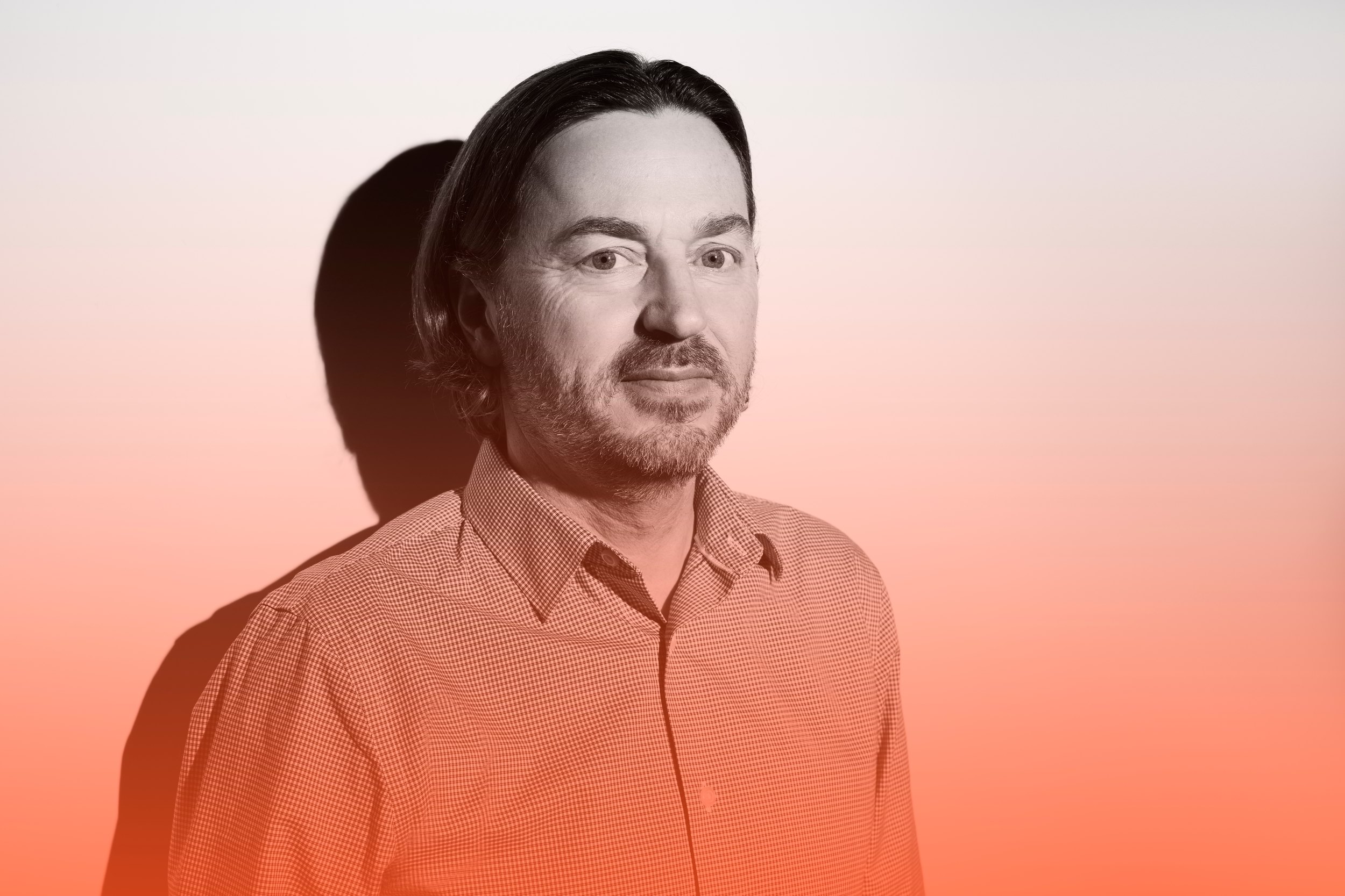 An innovator in a rust shirt, lit against a peach gradient