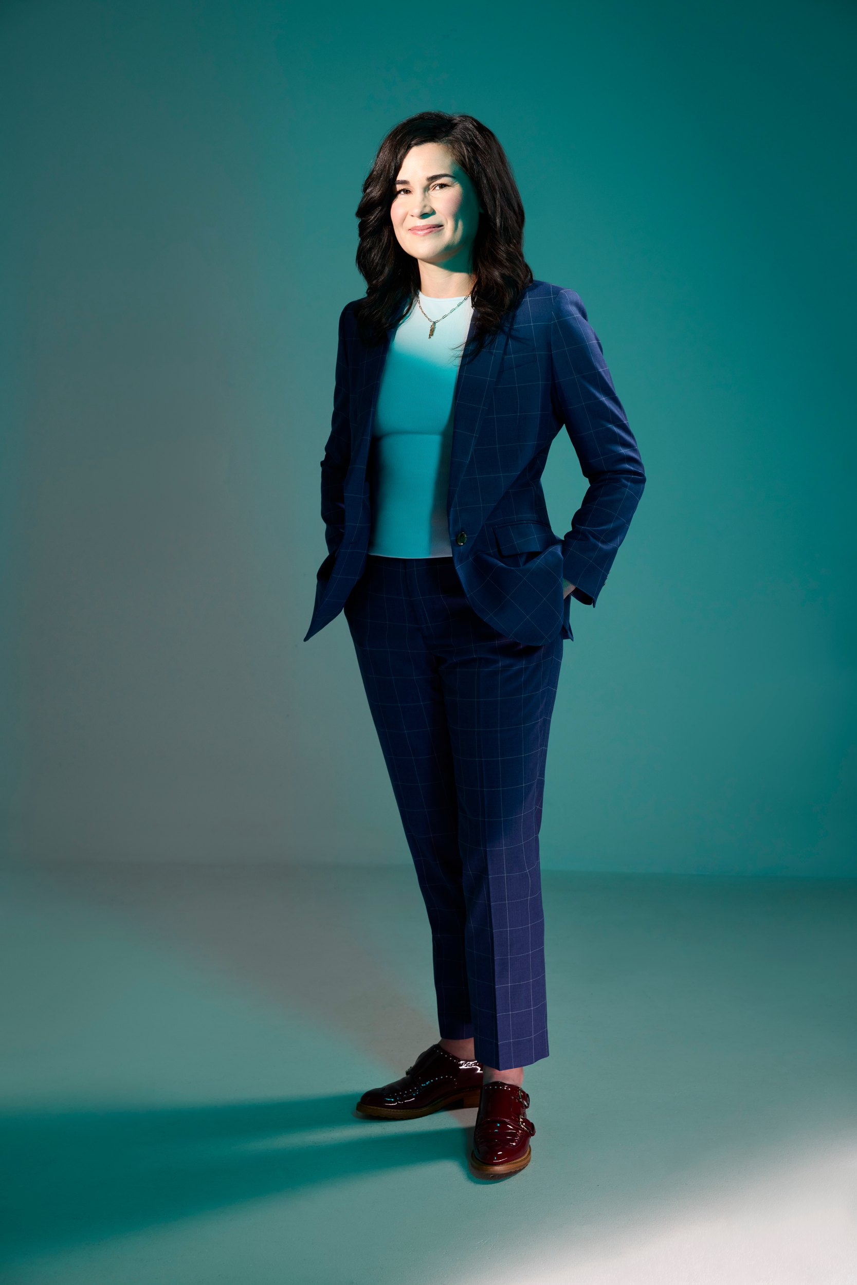 Dr. Blaire Anderson in a blue suit against teal, hands in her pockets