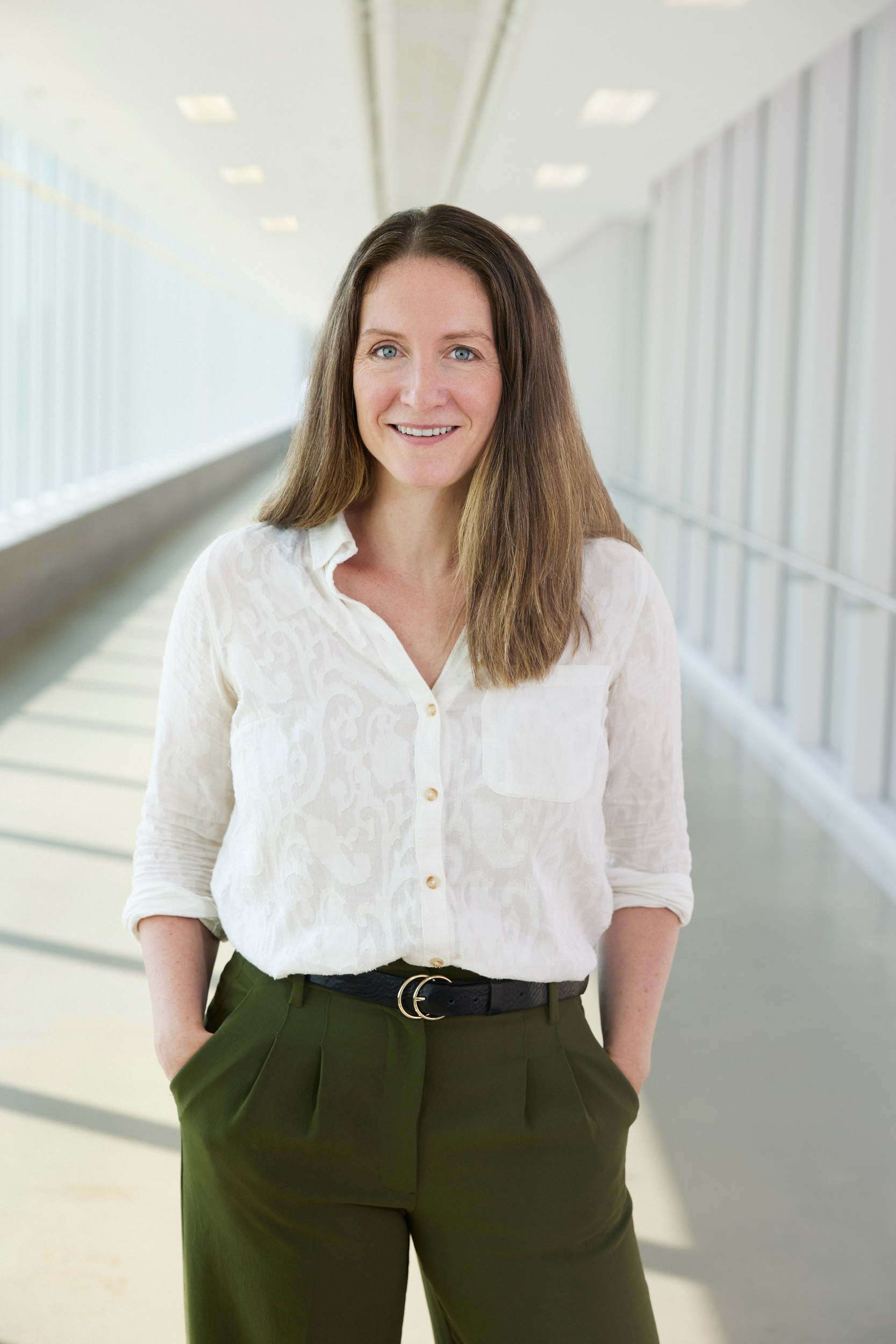Dr. Emily Walker in a glass corridor, hands in her pockets
