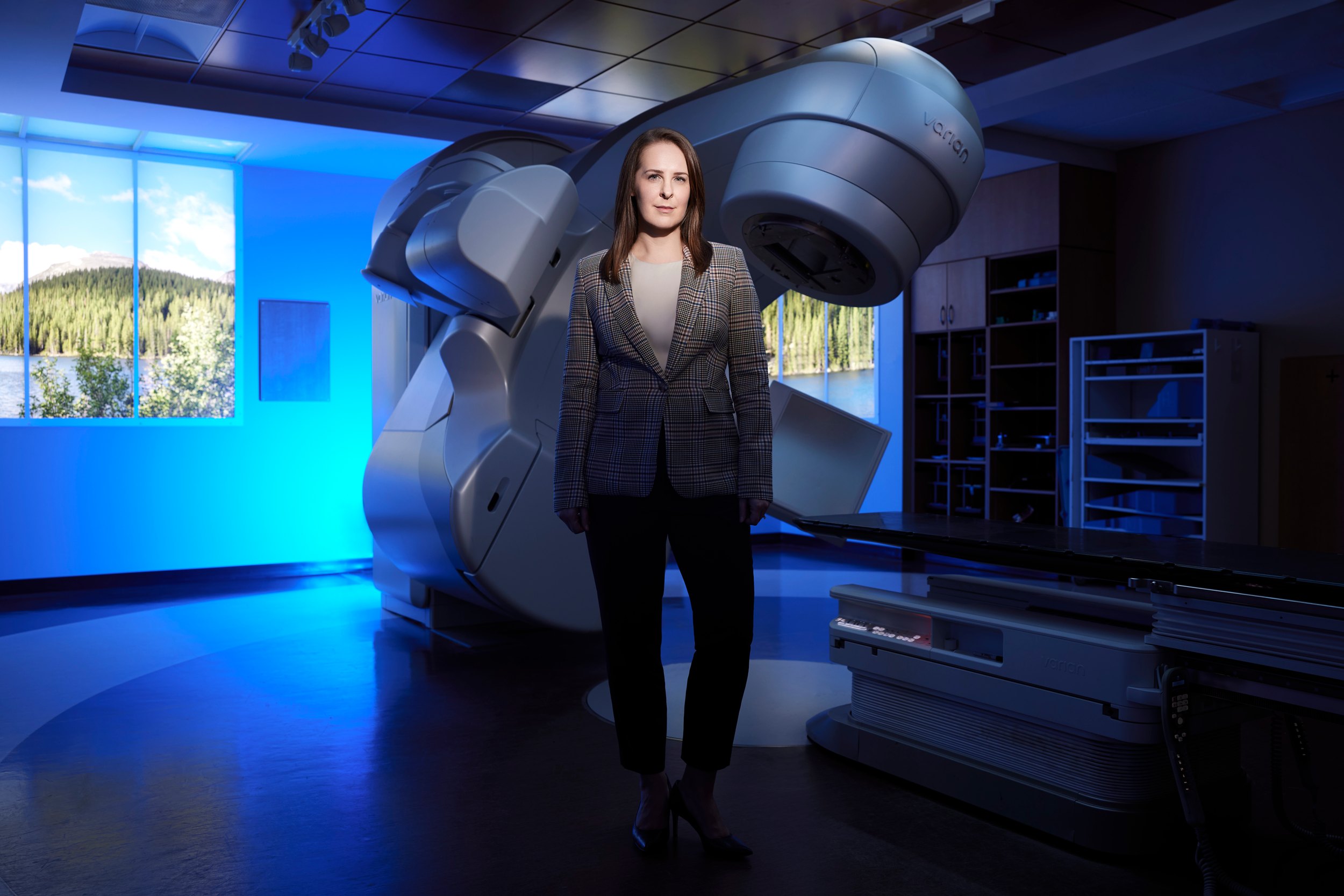 The room, wide: the physician small against the imaging machine, windows along the far wall