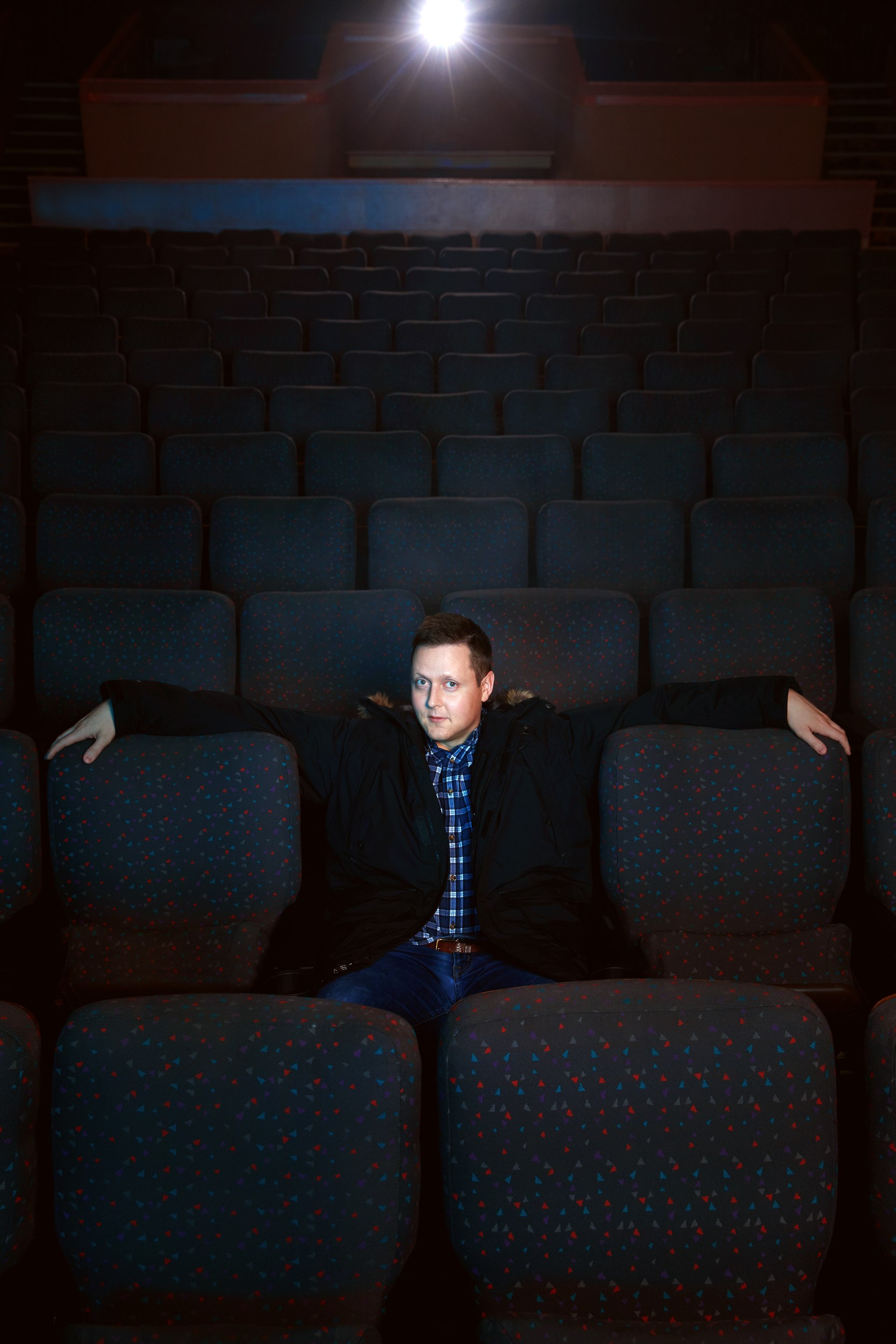 Arms out along the seats, the projector light behind him