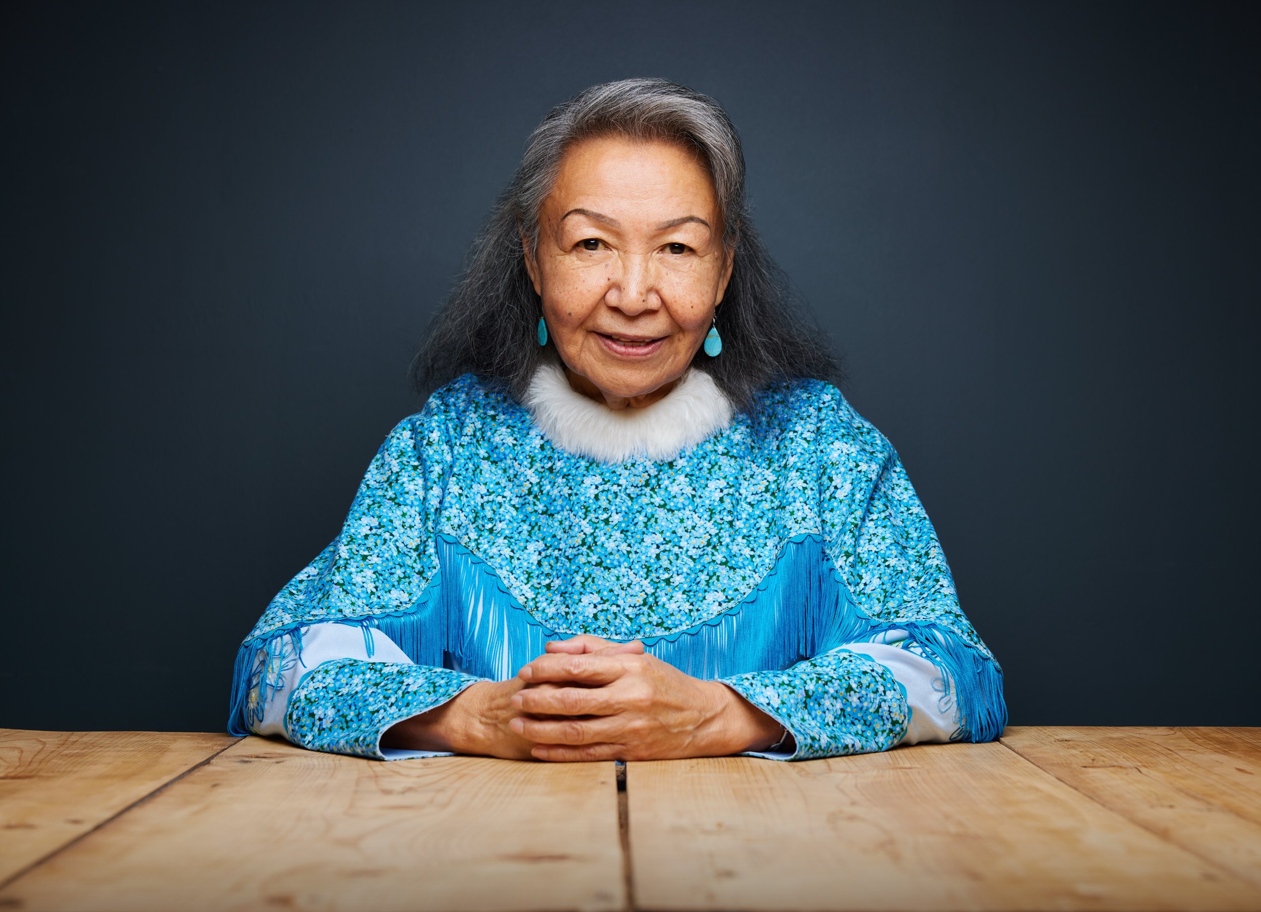 Leadership portrait: seated at a wooden table in a blue beaded dress