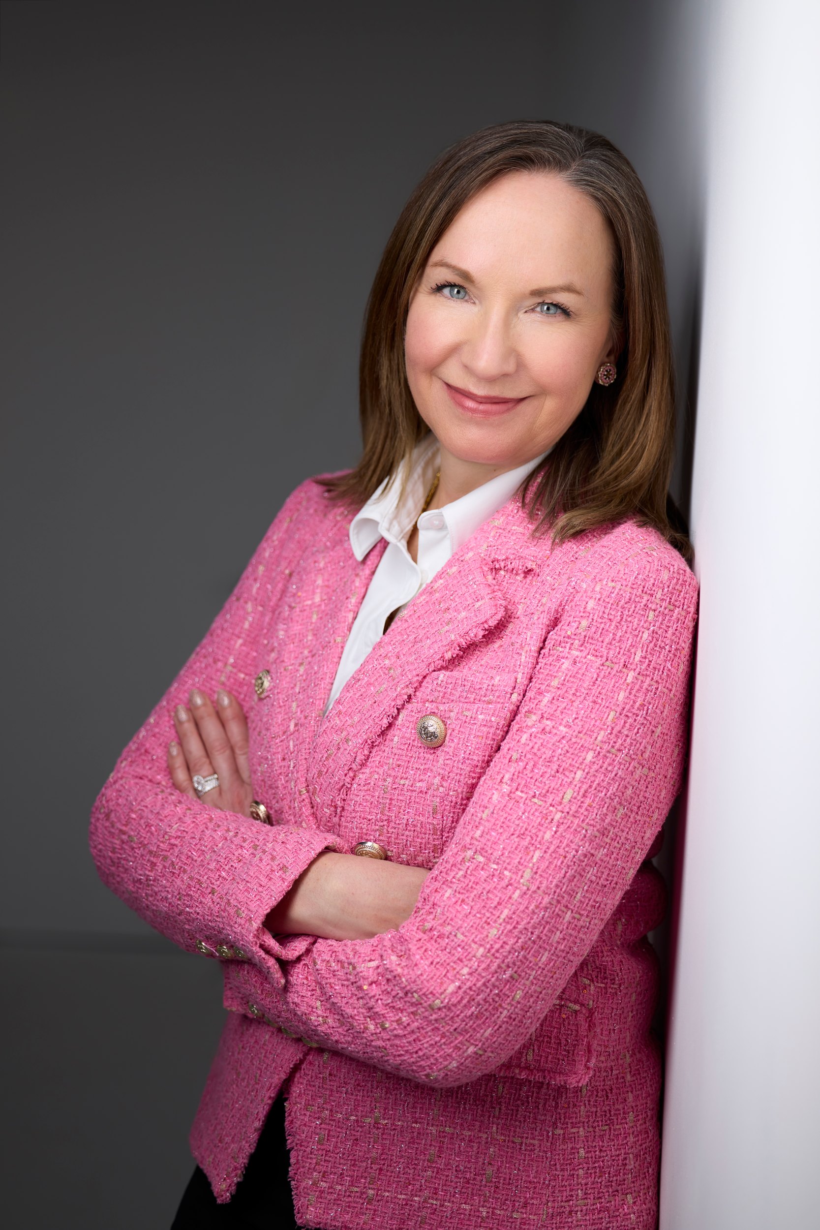 Leadership portrait: a pink blazer, arms crossed, against a wall of light