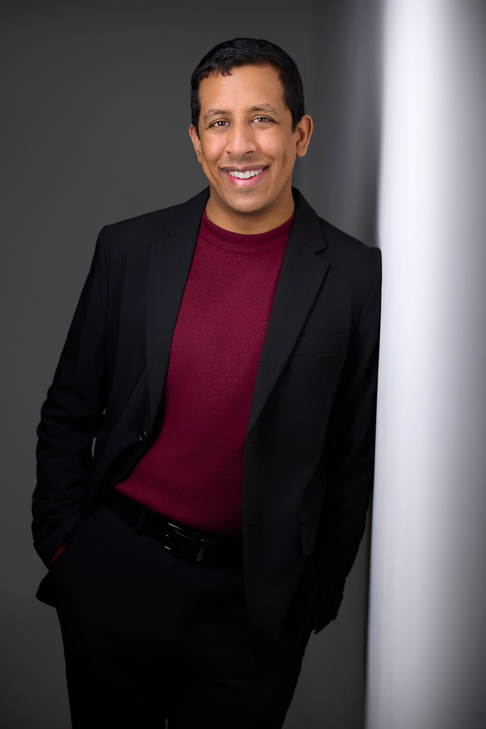 Leadership portrait: a black jacket and a burgundy sweater against a wall of light