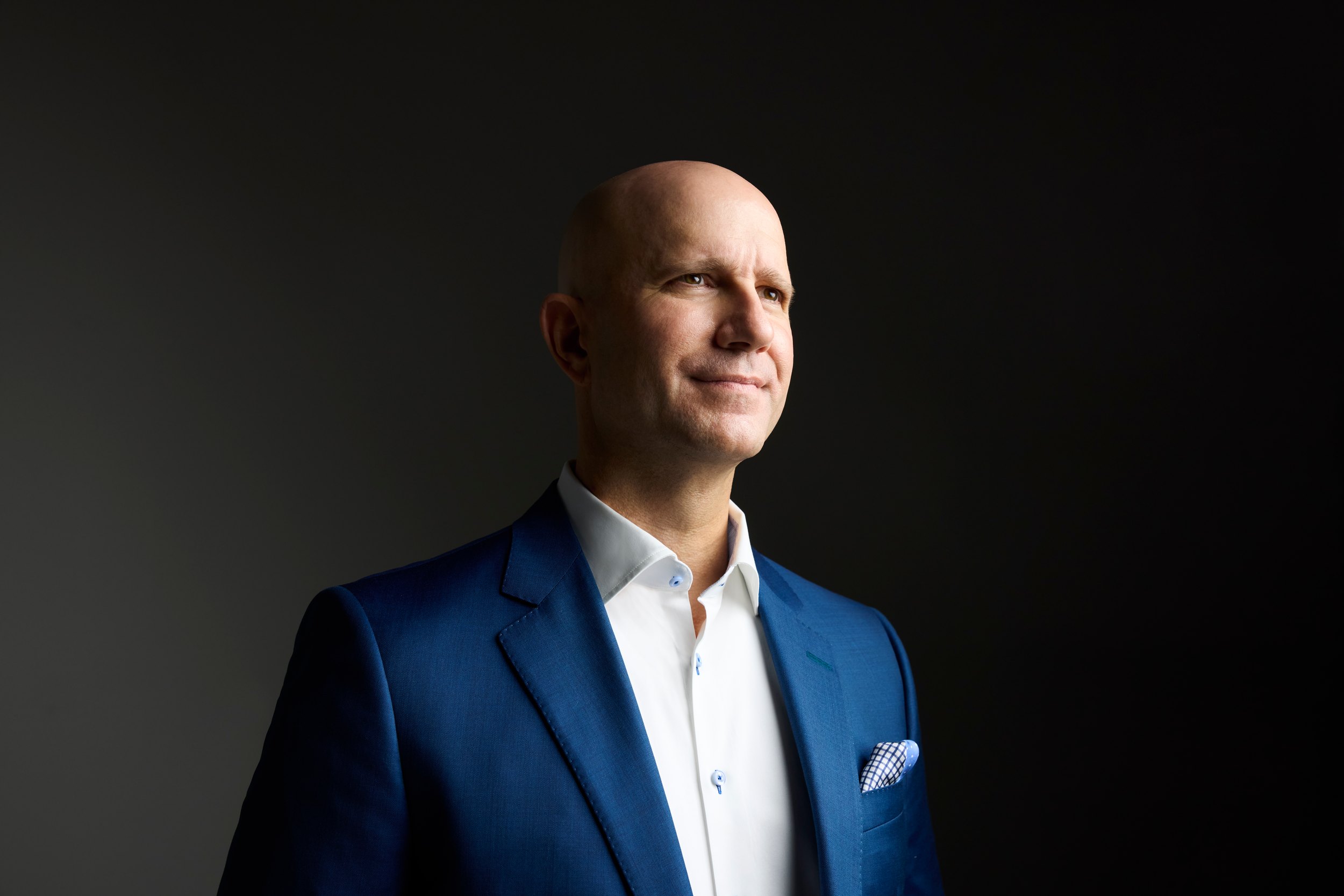 Leadership portrait: a navy suit, looking off, against charcoal