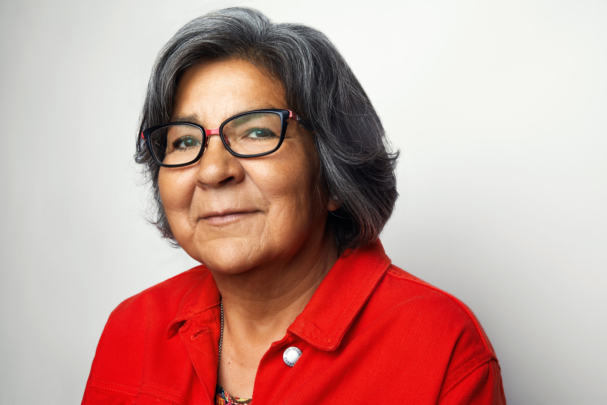 Leadership portrait: grey hair, glasses, a red jacket, close against white