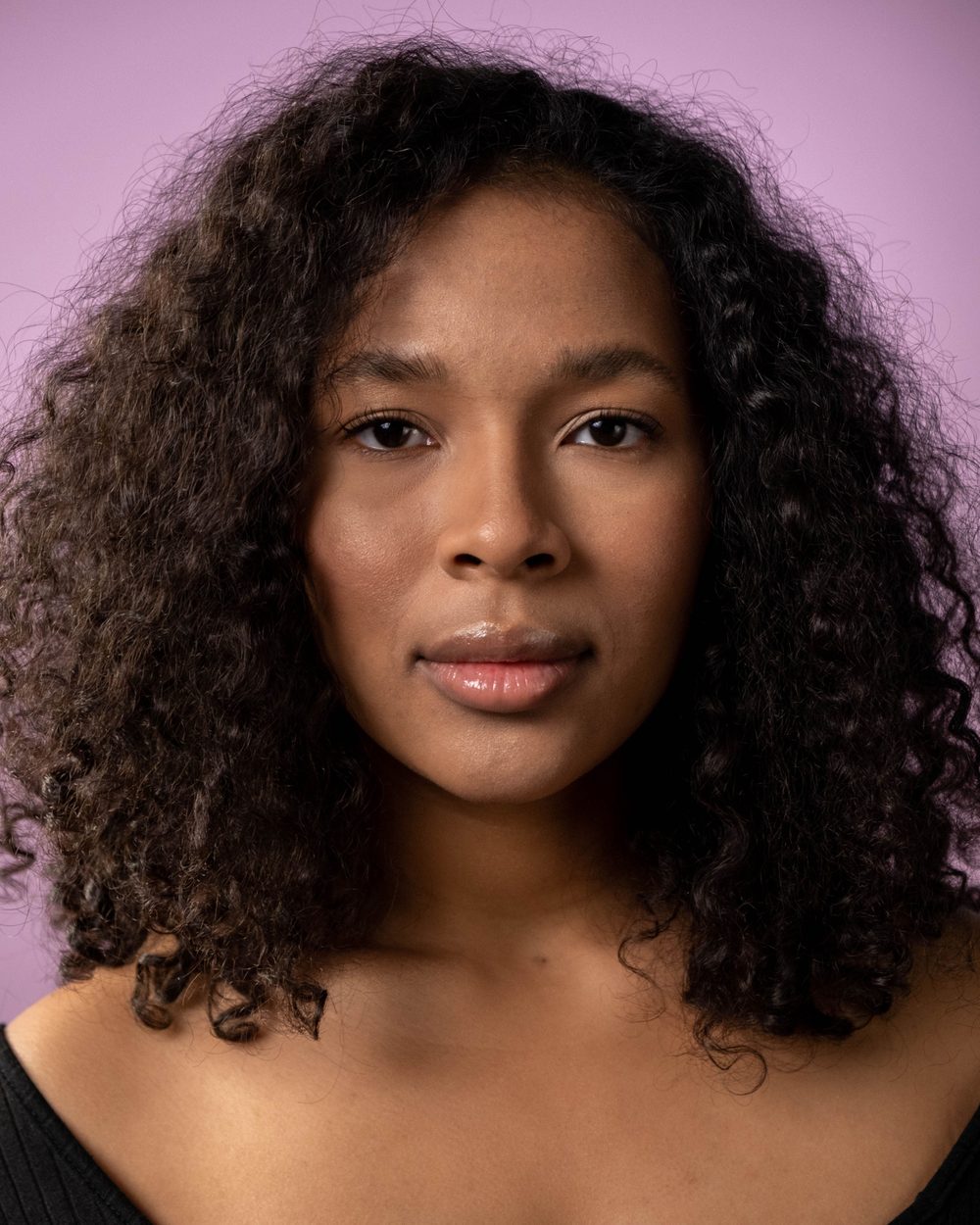 Real photo: a woman with long dark curls and a black top, against a pink backdrop