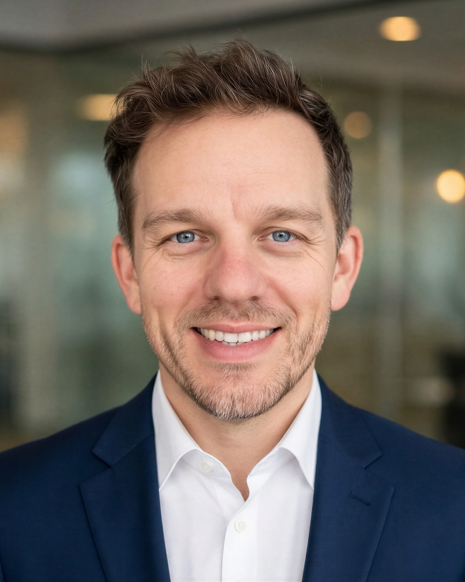 AI-generated headshot made from Ryan Parker’s selfies: a big even smile, a navy blazer and white shirt, in a glass-walled office