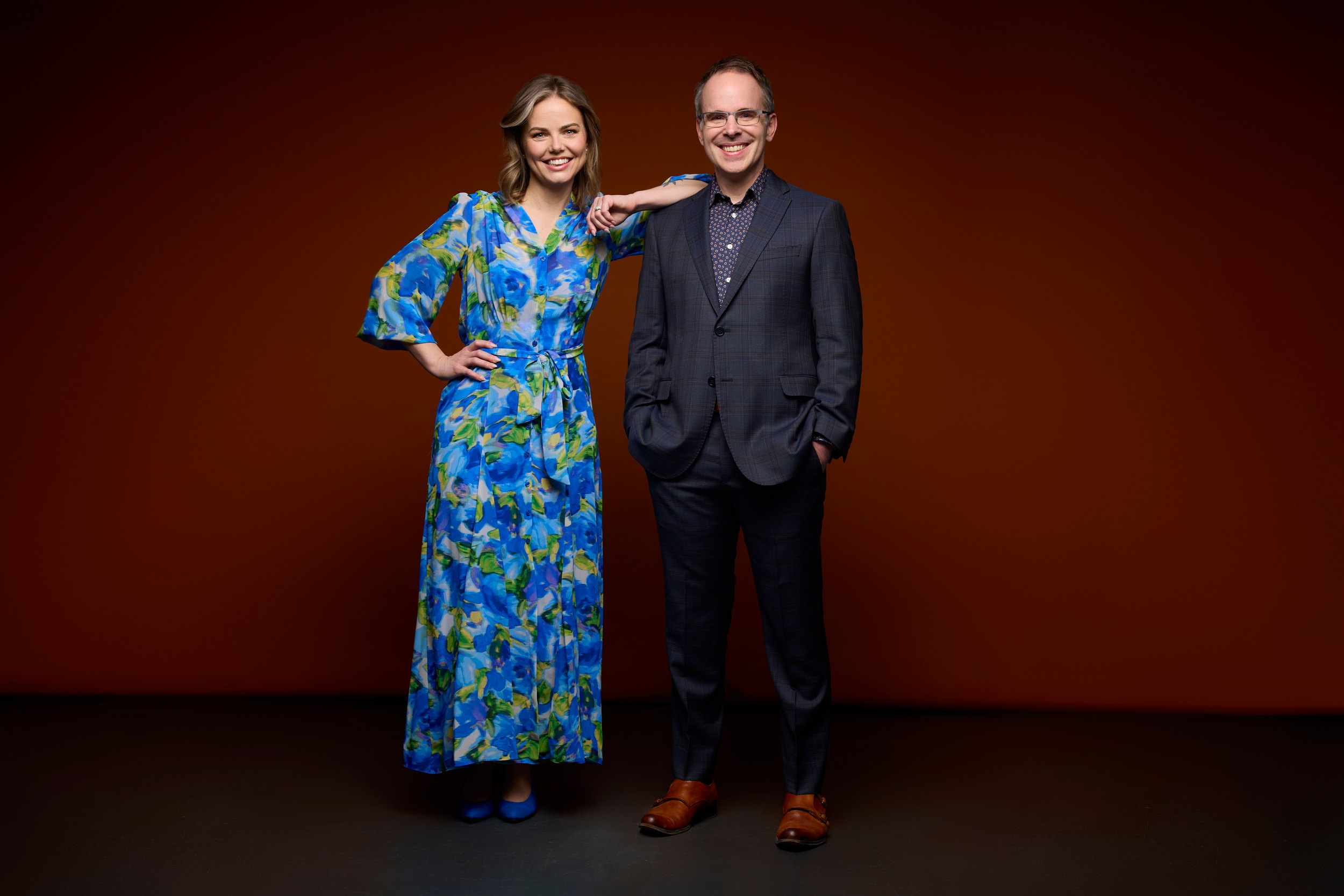 Two colleagues standing, on a warm brown backdrop