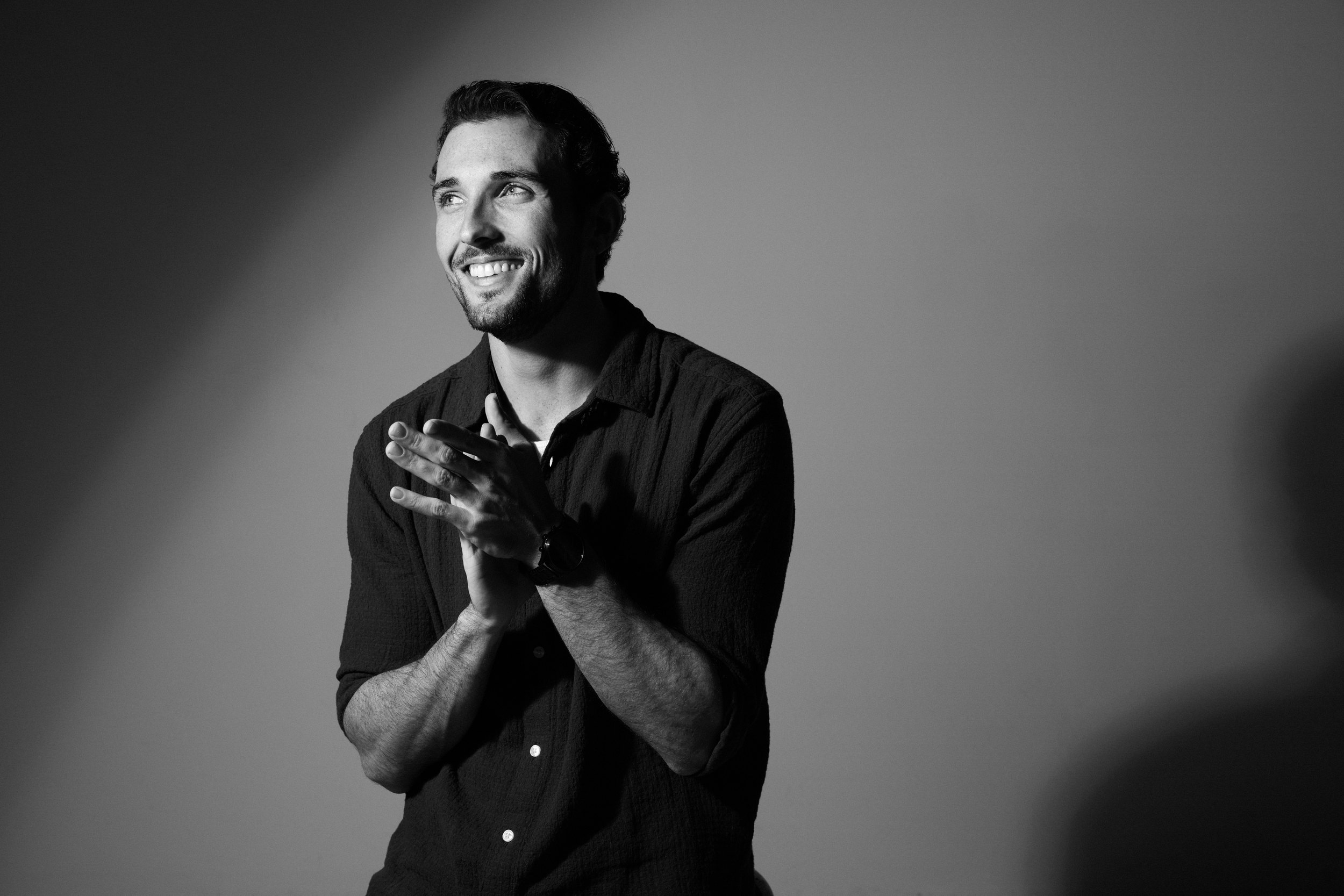 Content creator portrait in black and white: laughing, hands clasped, in a pool of light on grey, Edmonton studio