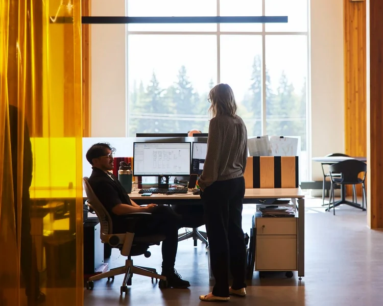Two colleagues at a desk behind an orange glass partition