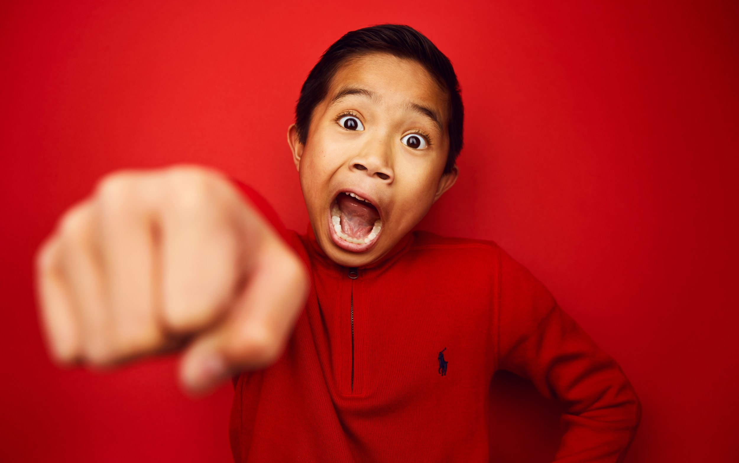 Kids headshot: a boy in a red shirt against a red backdrop, fist at the lens and mouth wide open, Edmonton studio