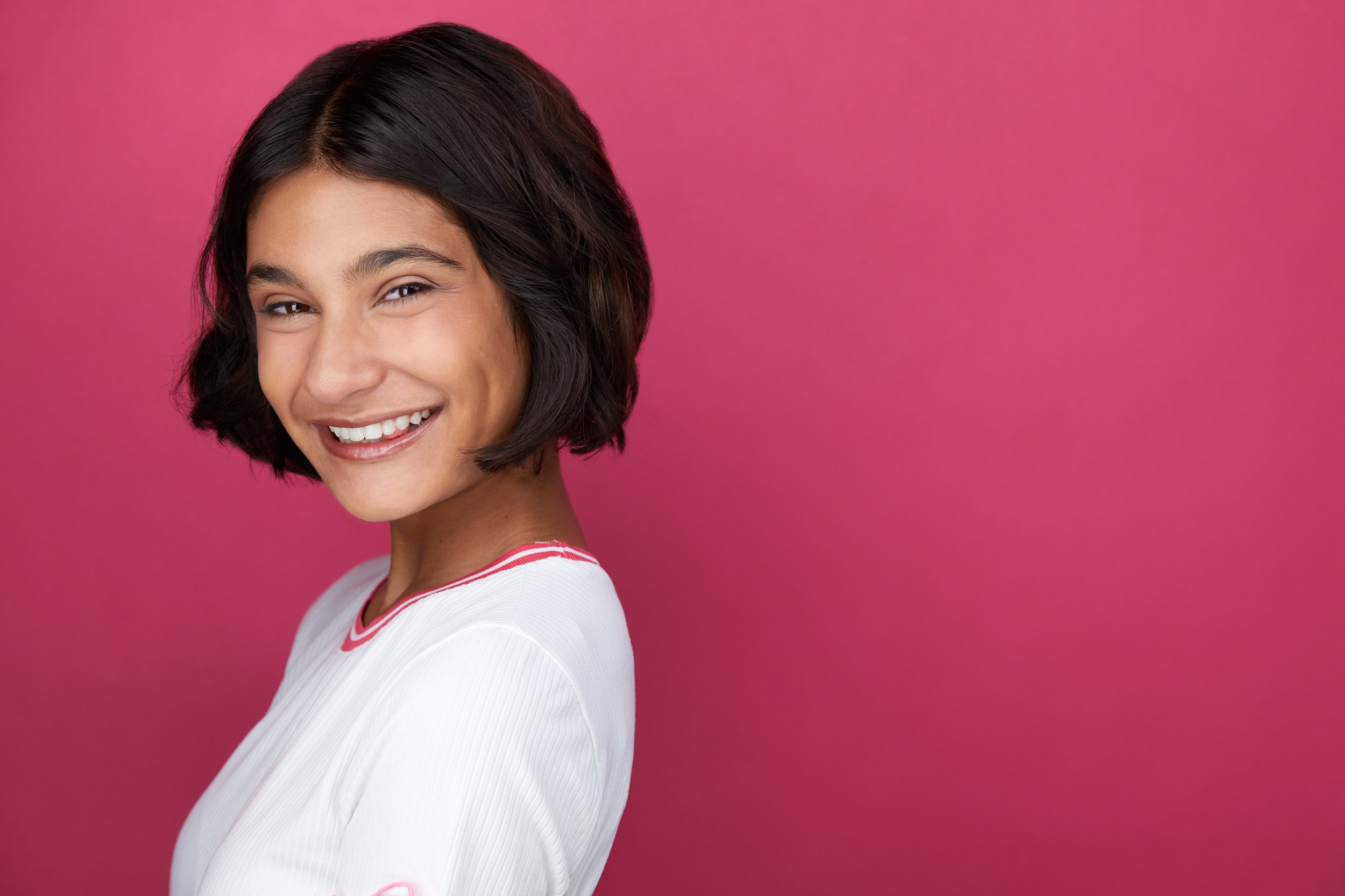 Kids and teens headshot: a white top against hot pink, a dark bob, laughing