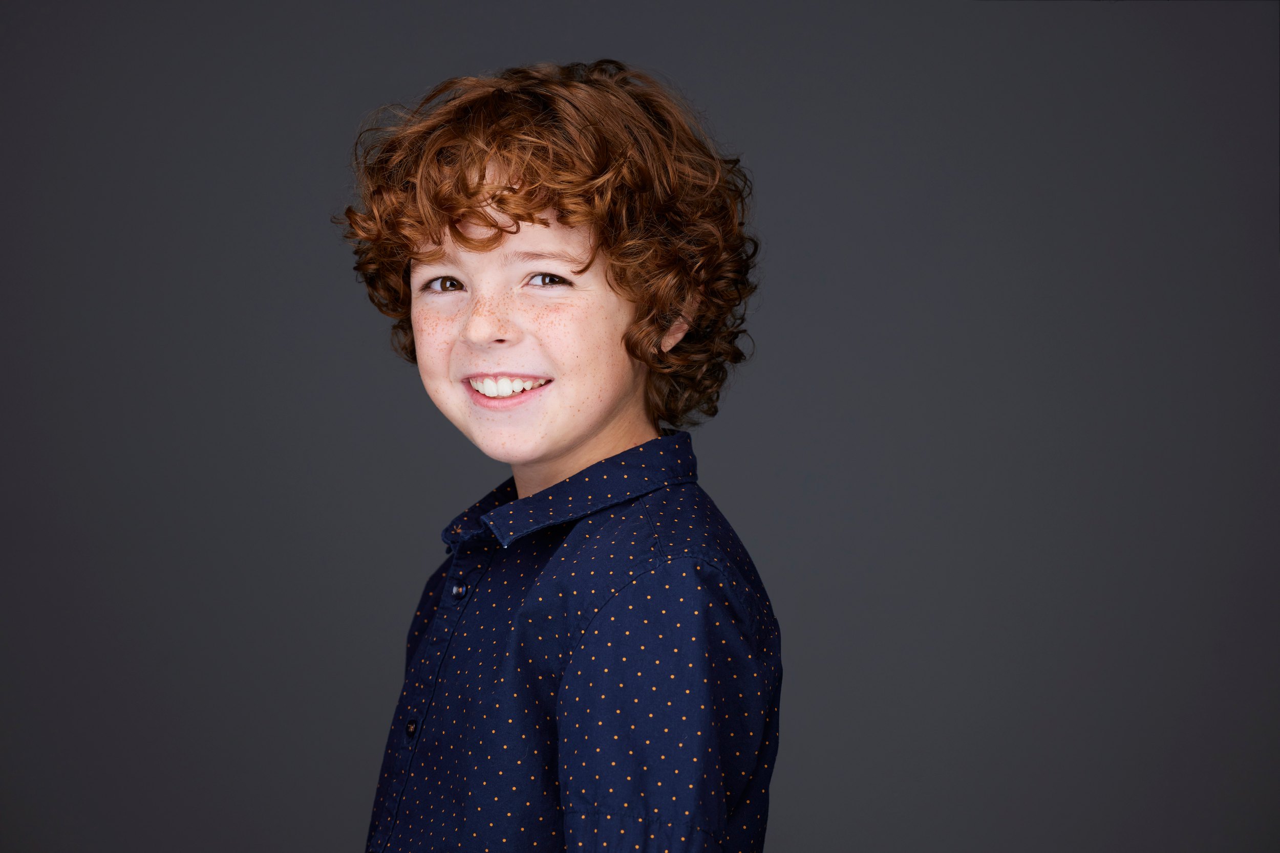 The same session, the navy polka-dot shirt against charcoal, grinning