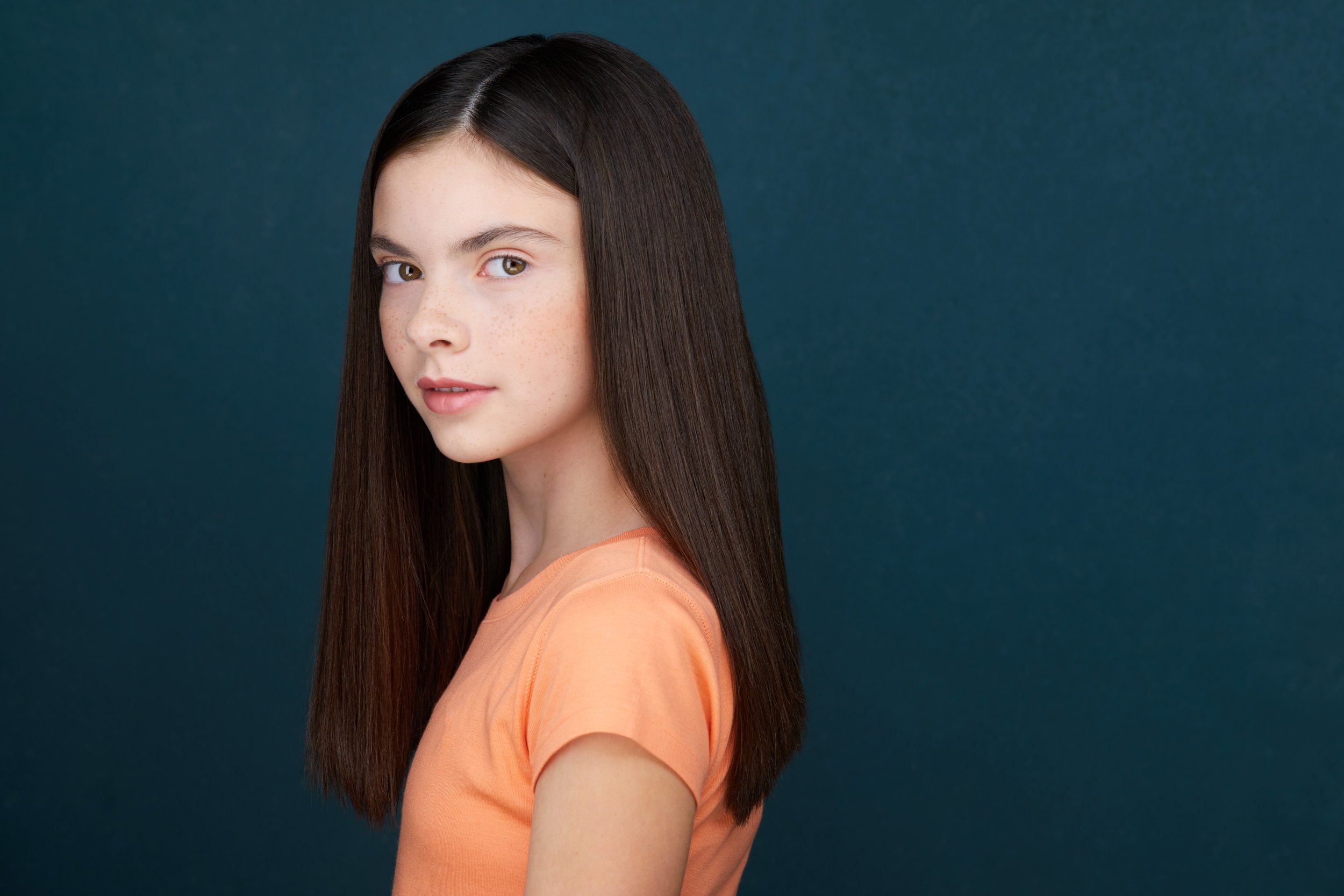 Kids and teens headshot: an orange top against teal, turned