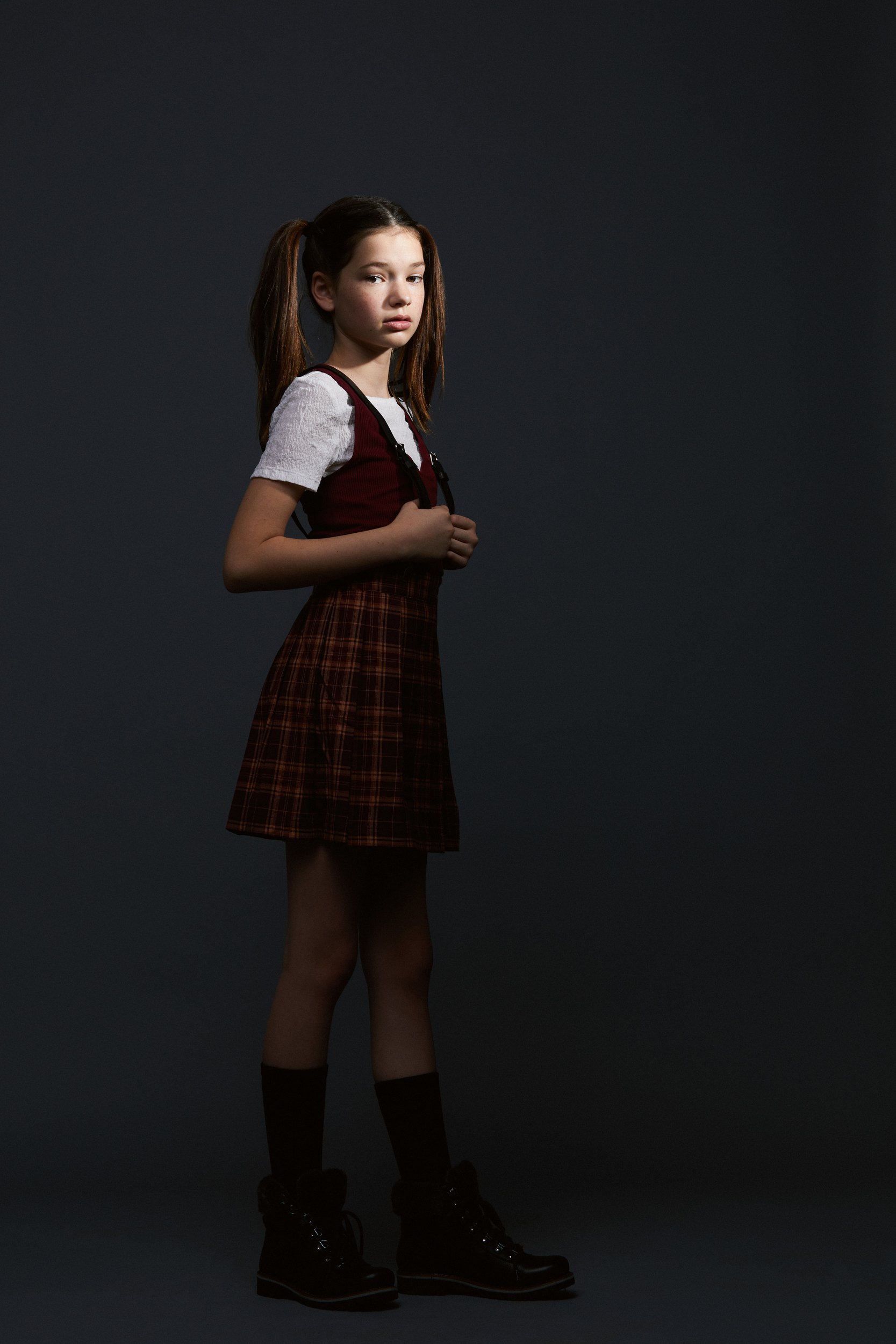 The same session, a plaid pinafore over a white tee, head to toe on grey