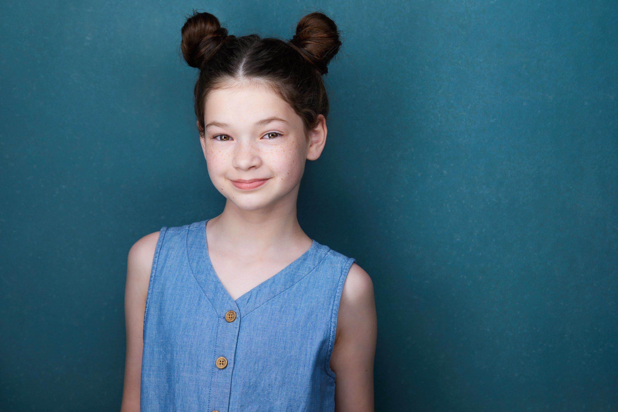 Kids and teens headshot: a blue top against teal, hair in two buns, smiling