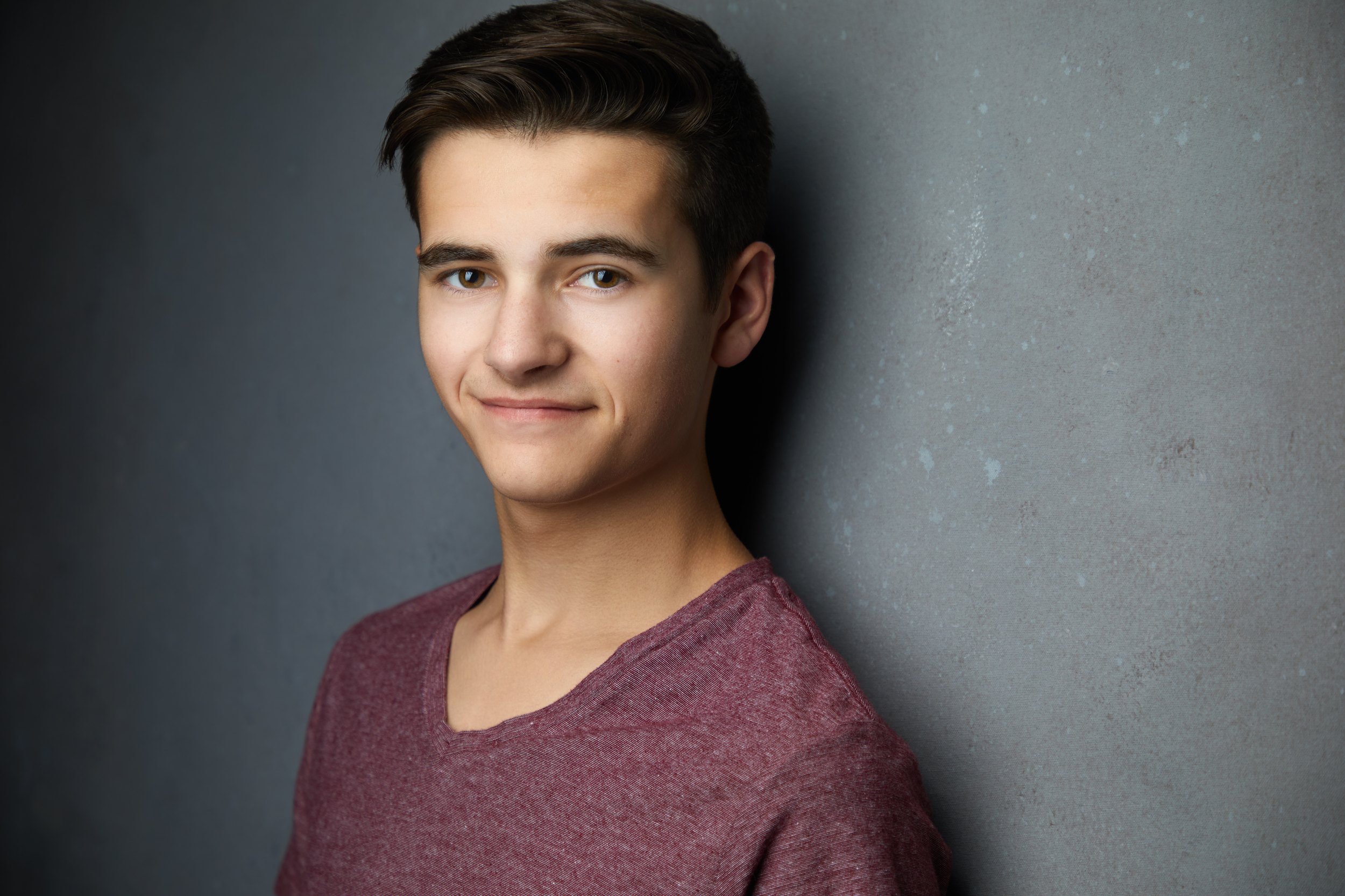 The same session, a maroon V-neck against a grey wall, smiling