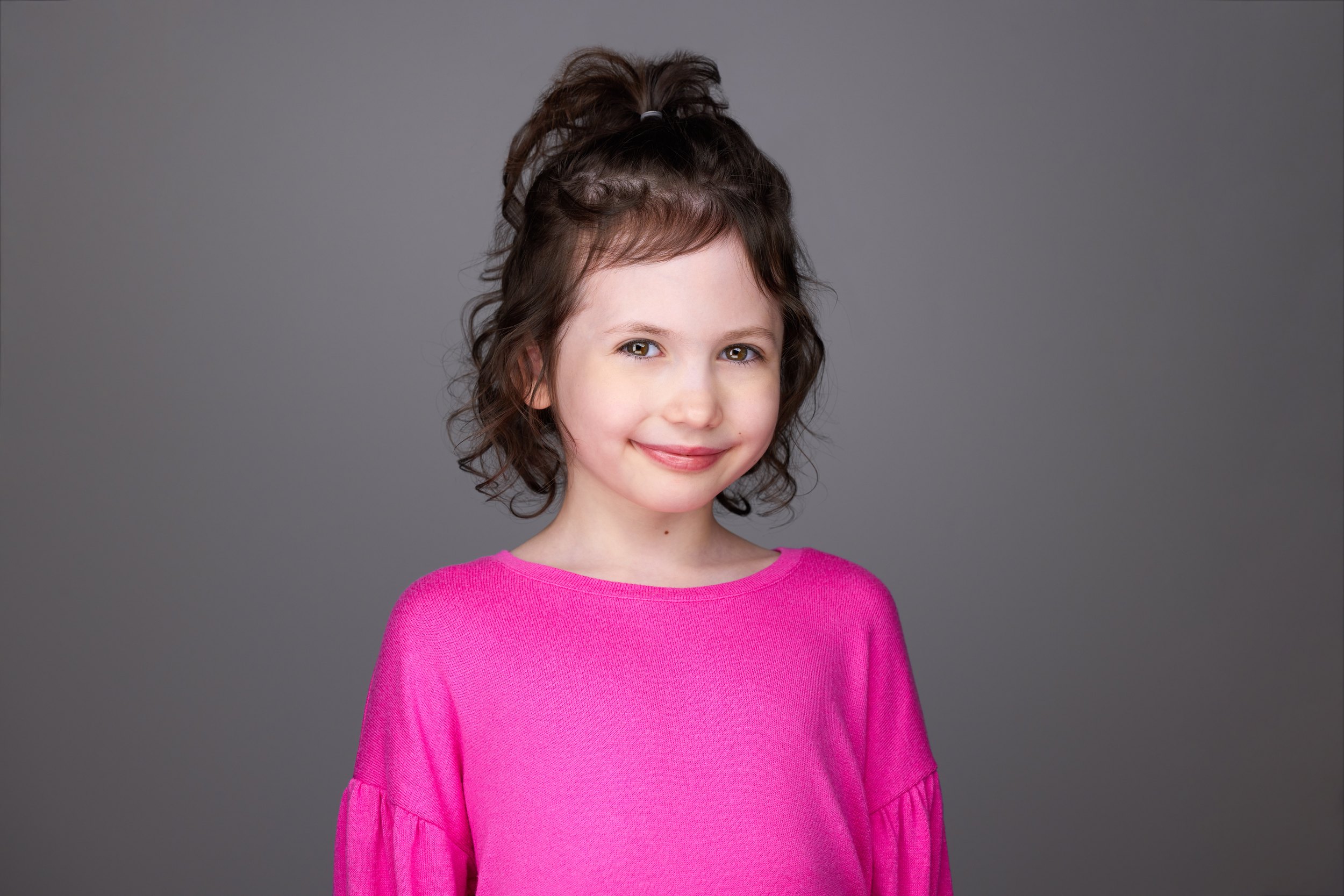 Kids and teens headshot: a pink top against grey, curls pinned up