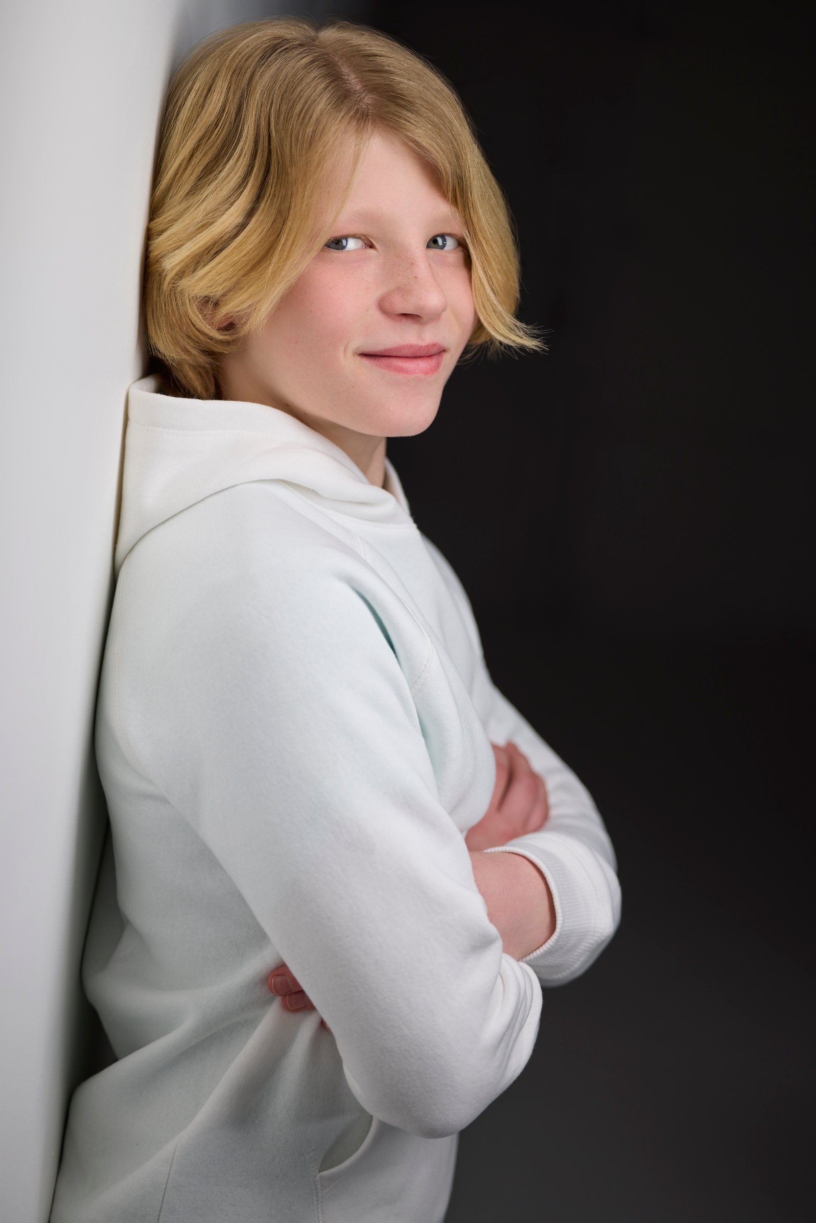 Kids and teens headshot: a white hoodie against the wall of light, arms crossed, looking up