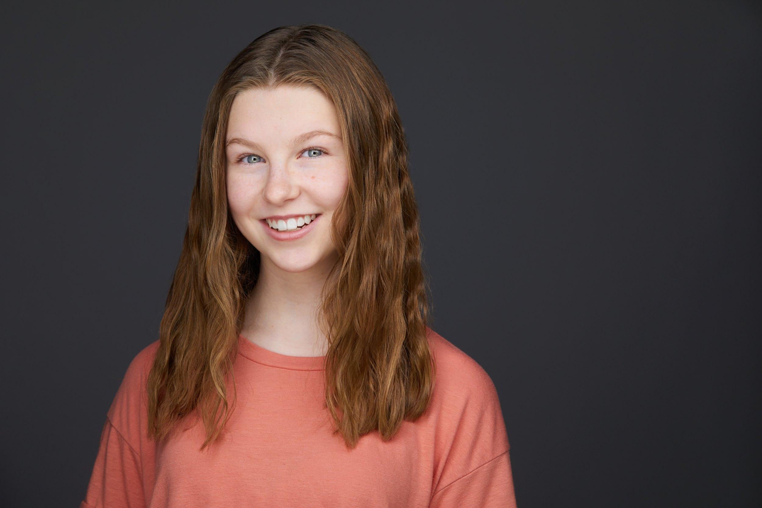 Kids and teens headshot: a coral sweater against grey, hair braided