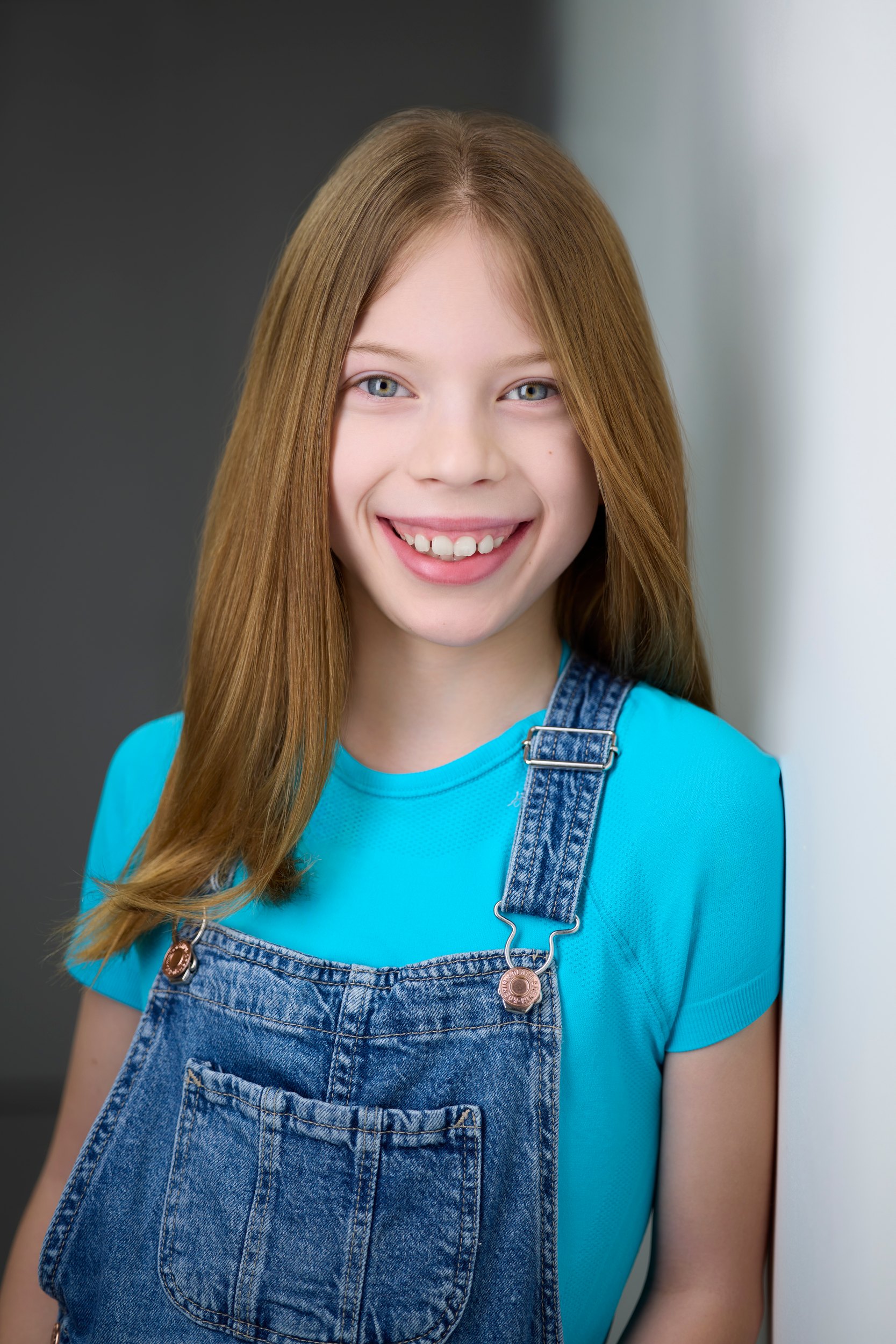 The same session, a teal tee and overalls, grinning