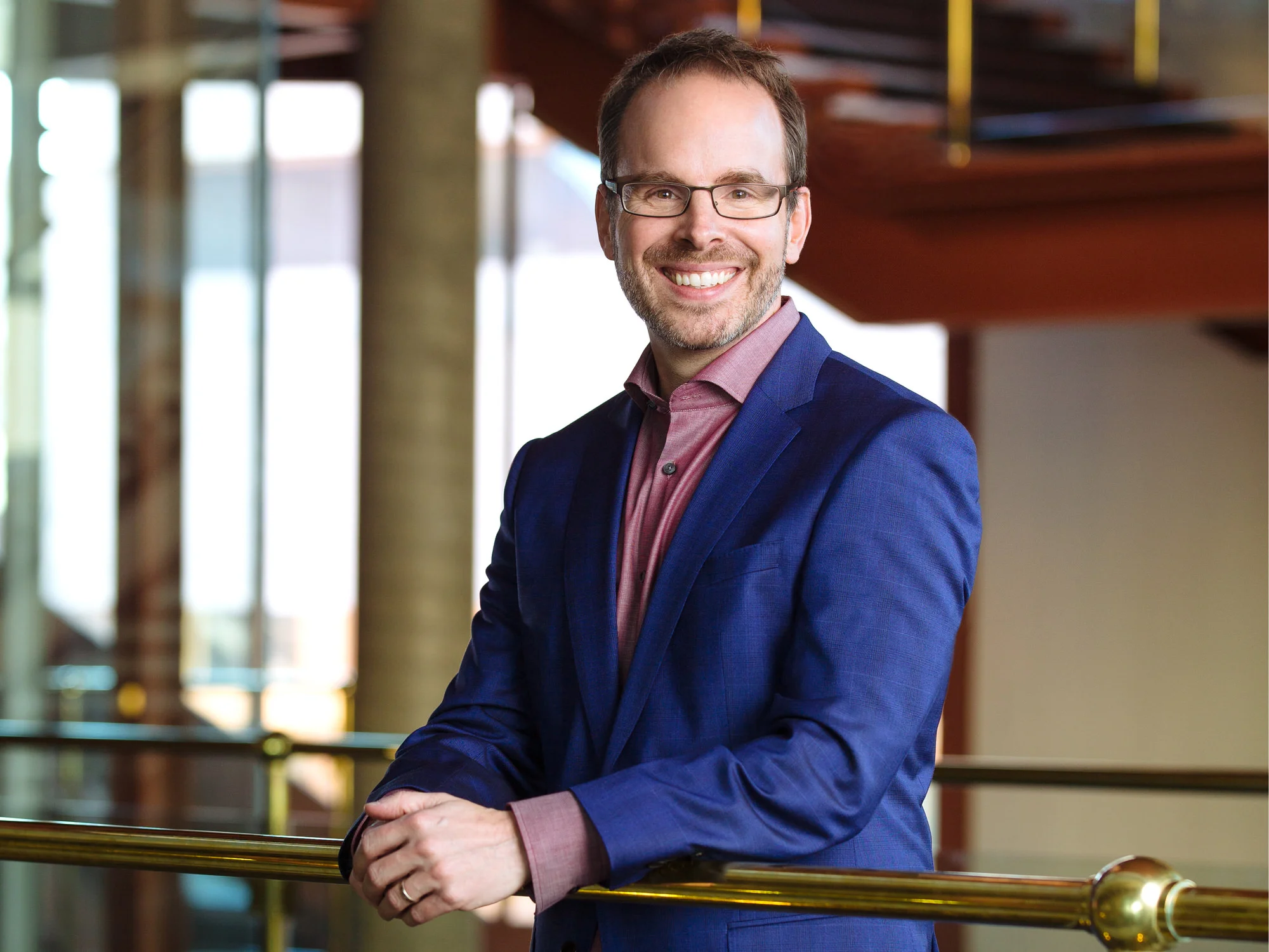 Portrait at a brass railing in a theatre lobby, blue suit