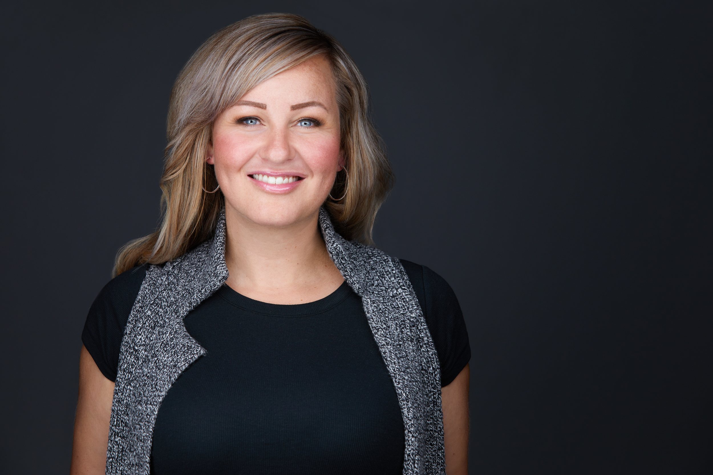 Real estate headshot: shoulder-length hair, a grey vest over black, on dark
