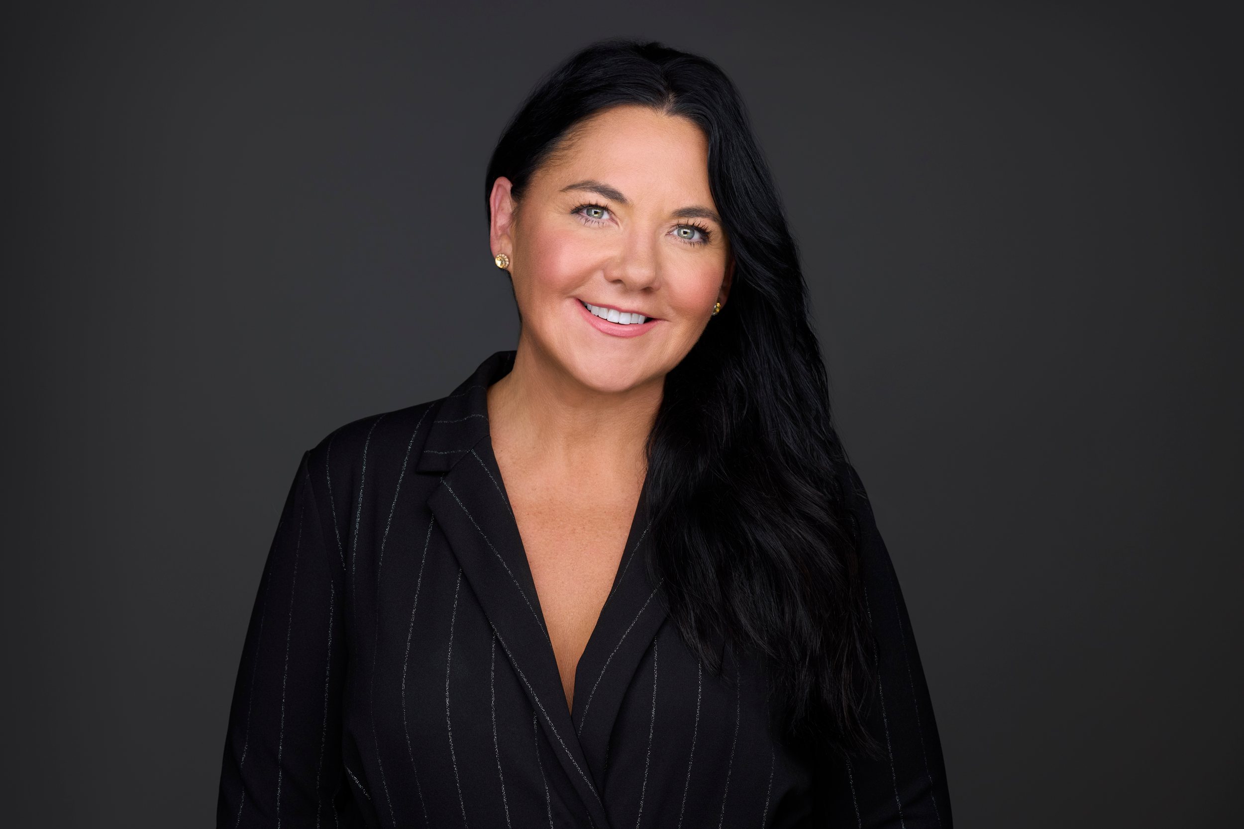 Real estate headshot: long dark hair, a black pinstripe blazer, on dark
