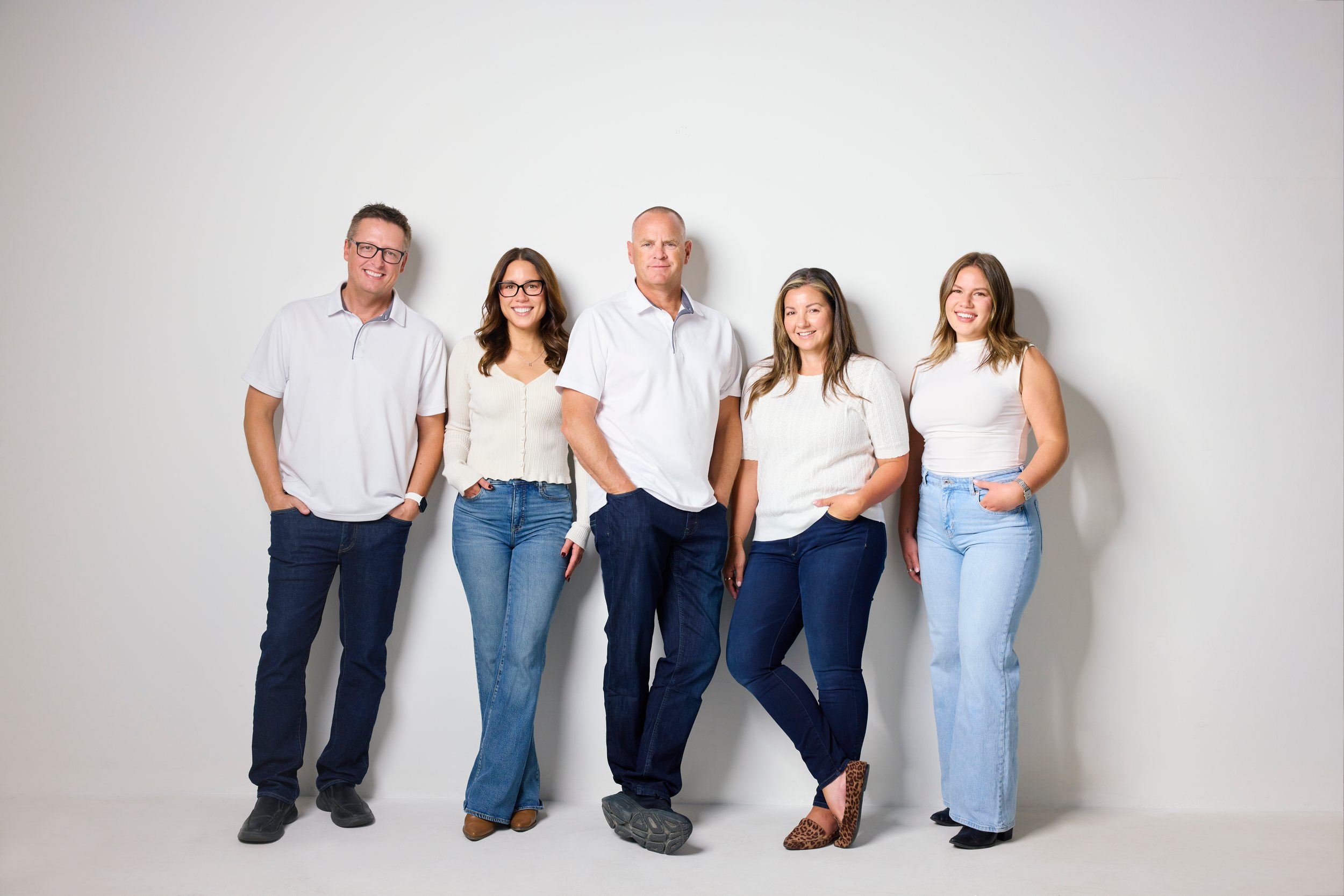 A real estate team of five standing full length on white, jeans and white shirts