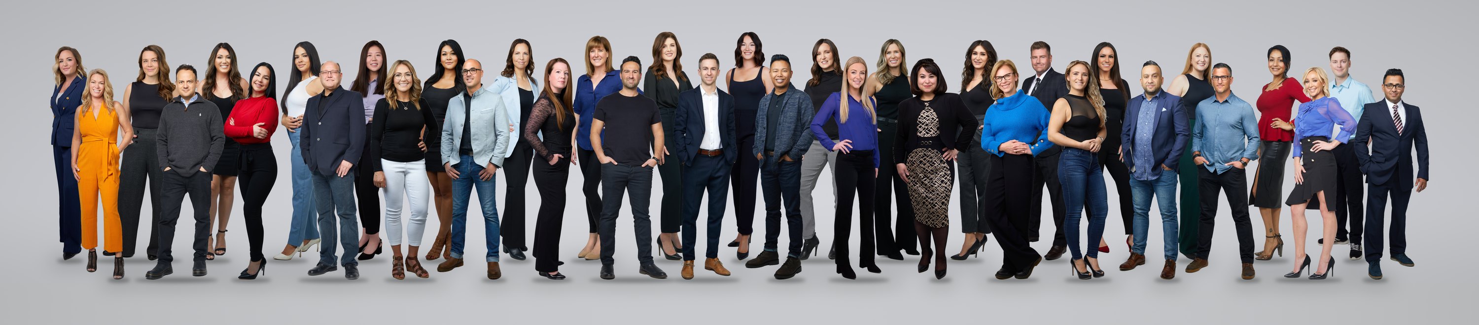 The same real estate office in one picture on light grey: thirty-six agents standing full length in two rows, suits, blazers, dresses and jeans