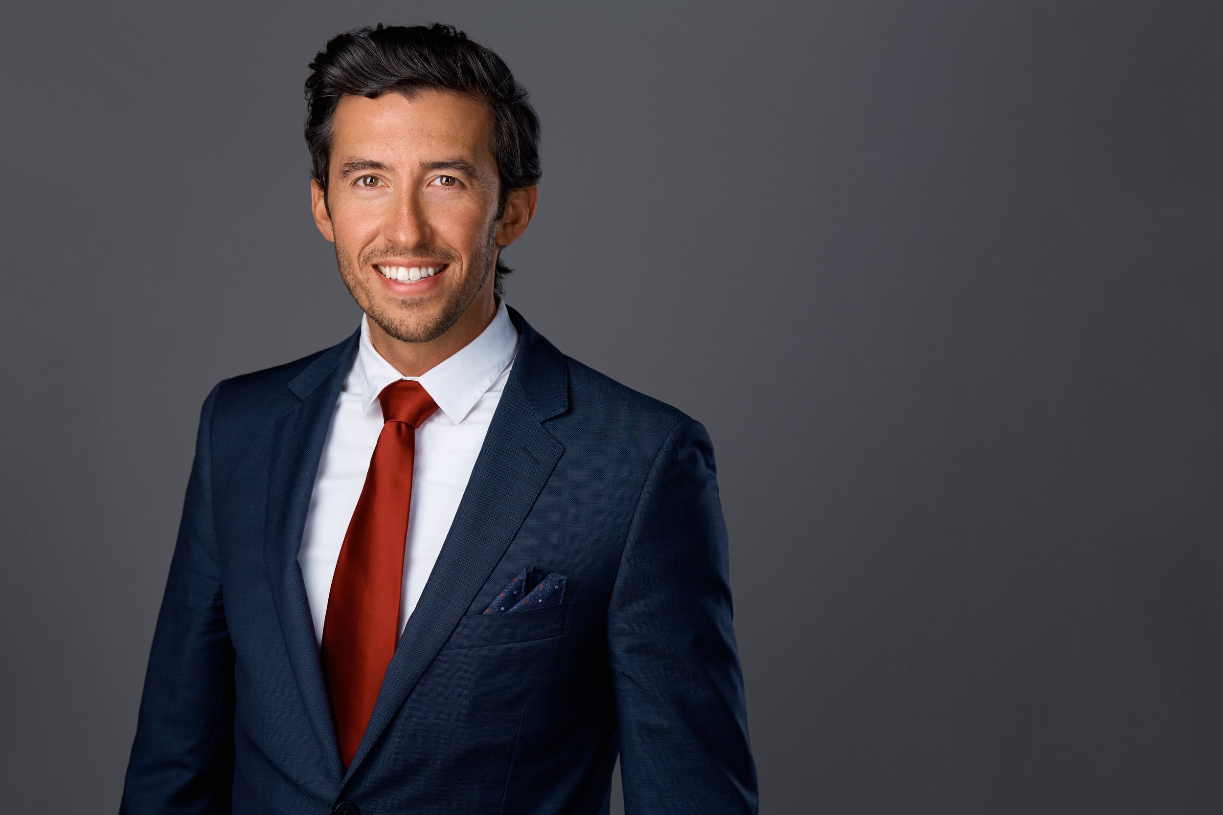 Mortgage broker headshot: a navy suit, white shirt and red tie, smiling, on dark grey