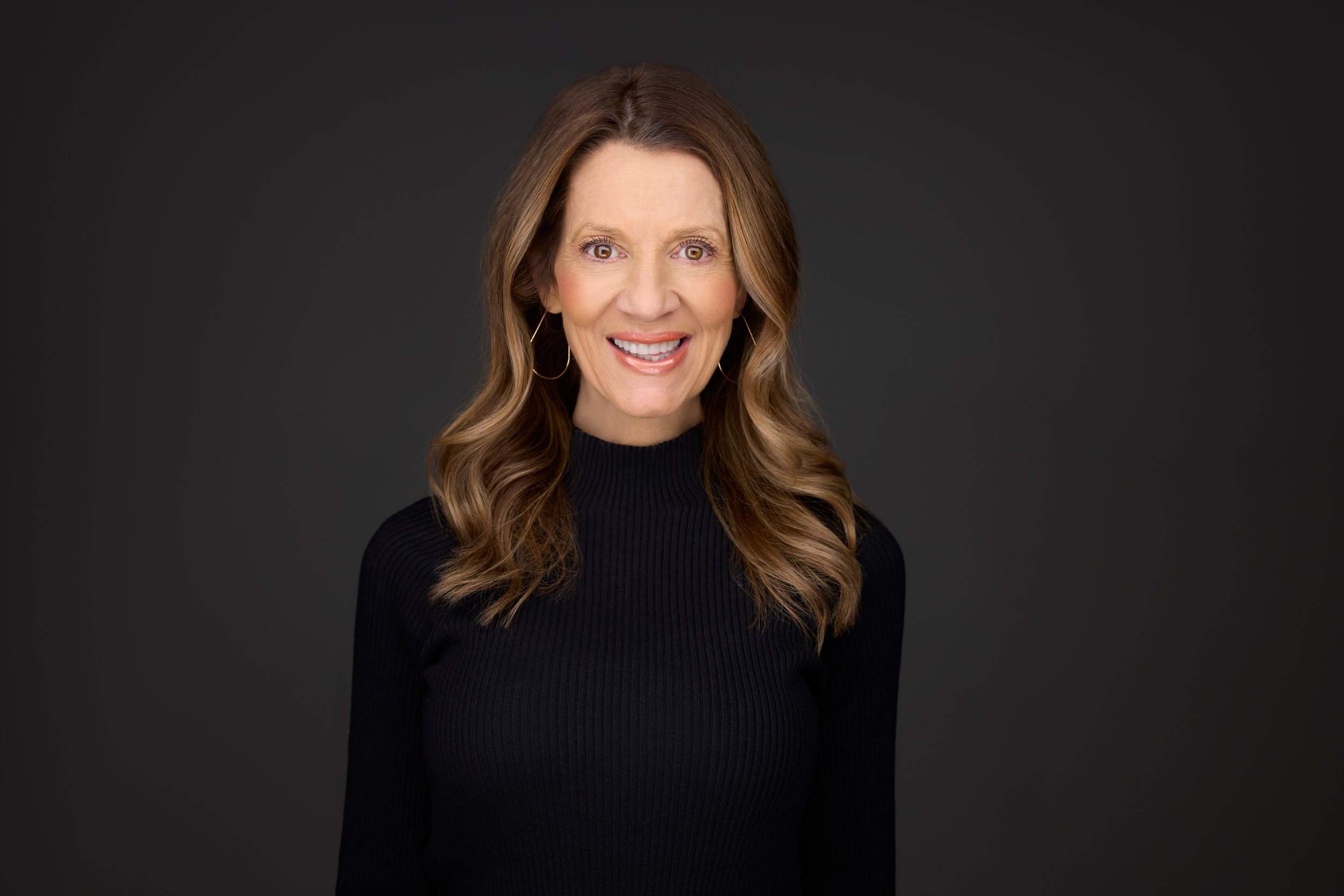 Real estate headshot: long highlighted hair, a black mock neck, on dark