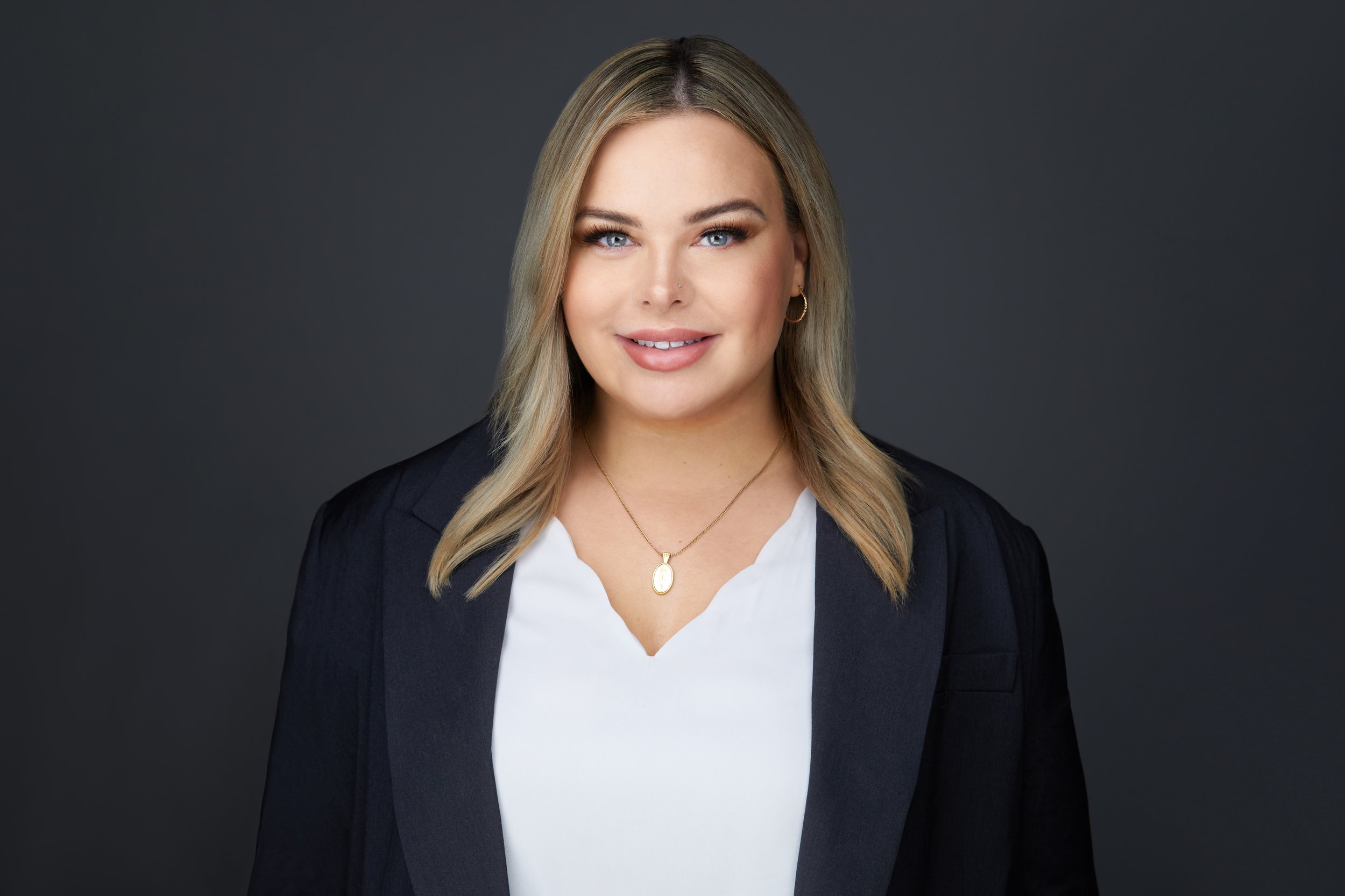 Real estate headshot: long blonde hair, a navy blazer over white, on dark grey