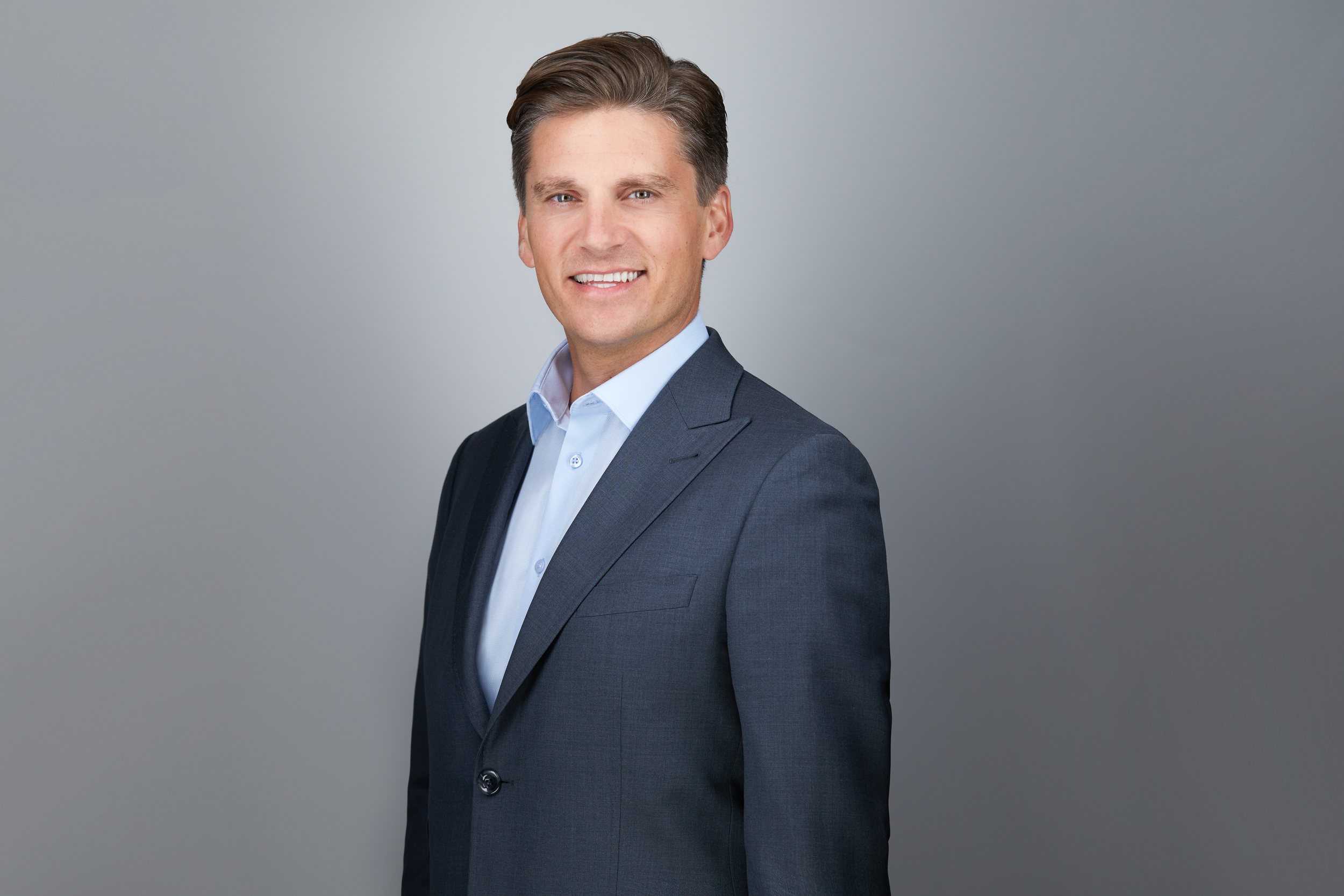 Real estate headshot: a grey suit and an open blue collar, smiling, on grey