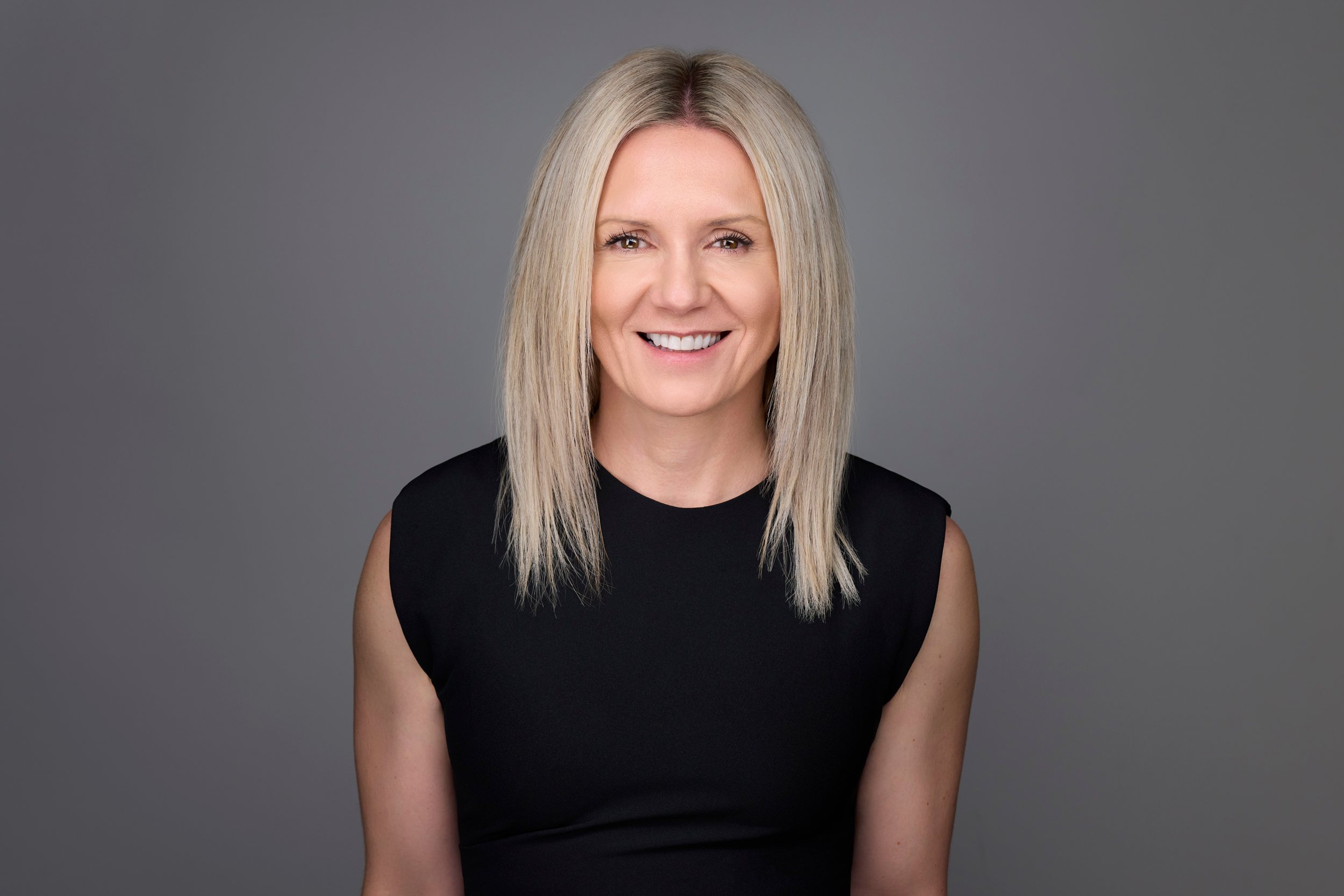 Real estate headshot: a platinum bob, a black sleeveless top, on mid grey