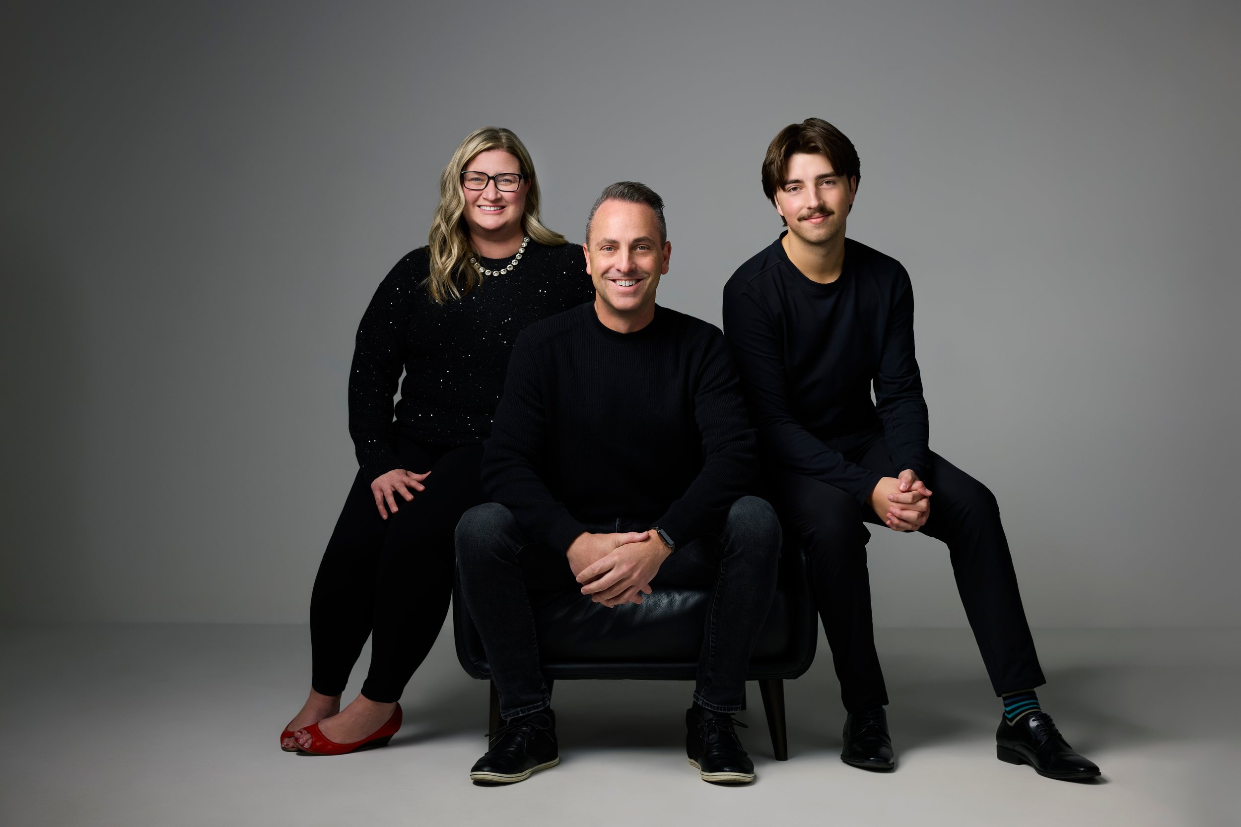 A realtor team of three dressed in black, one seated, on grey