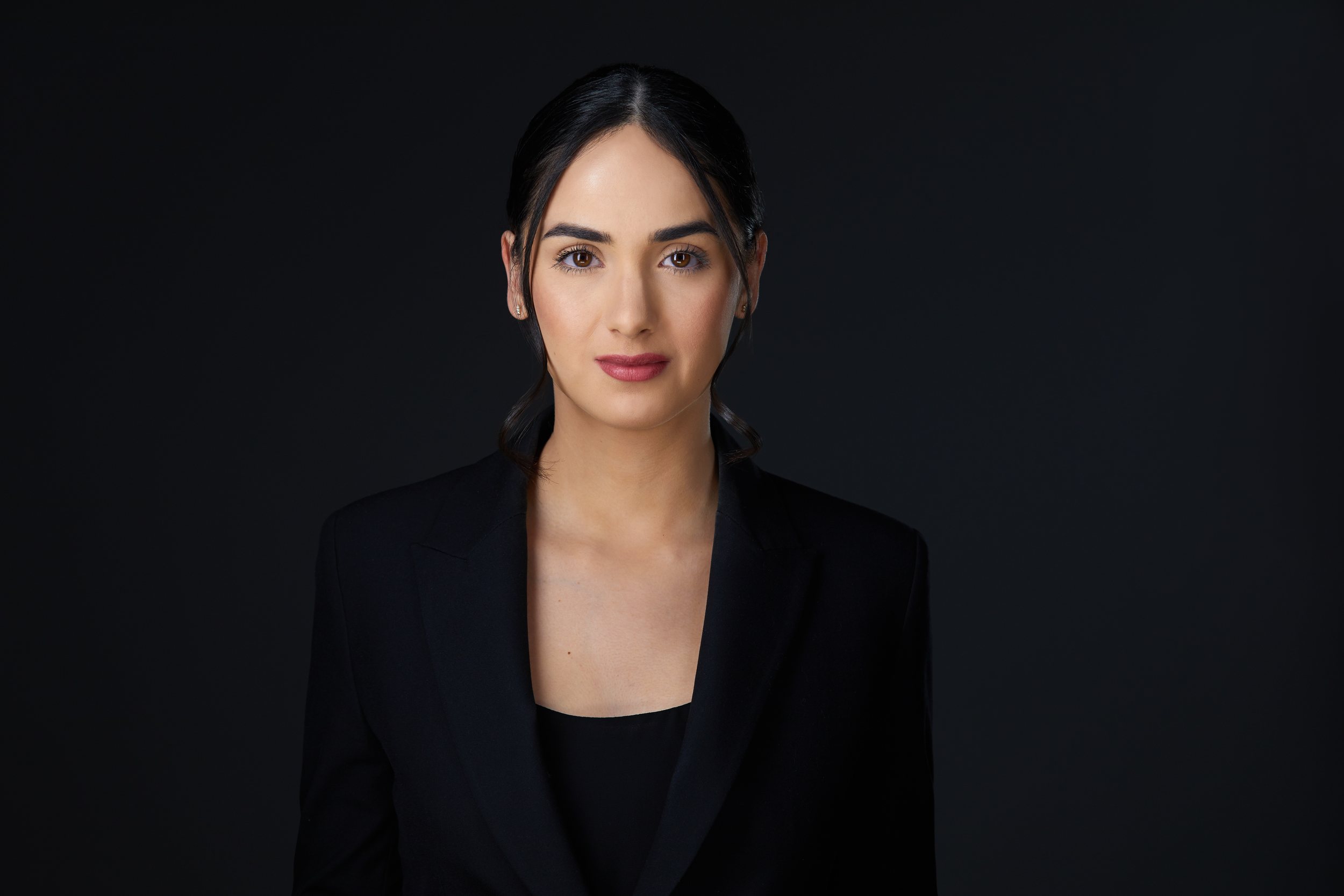 Real estate headshot: long dark hair pulled back, a black blazer, on dark