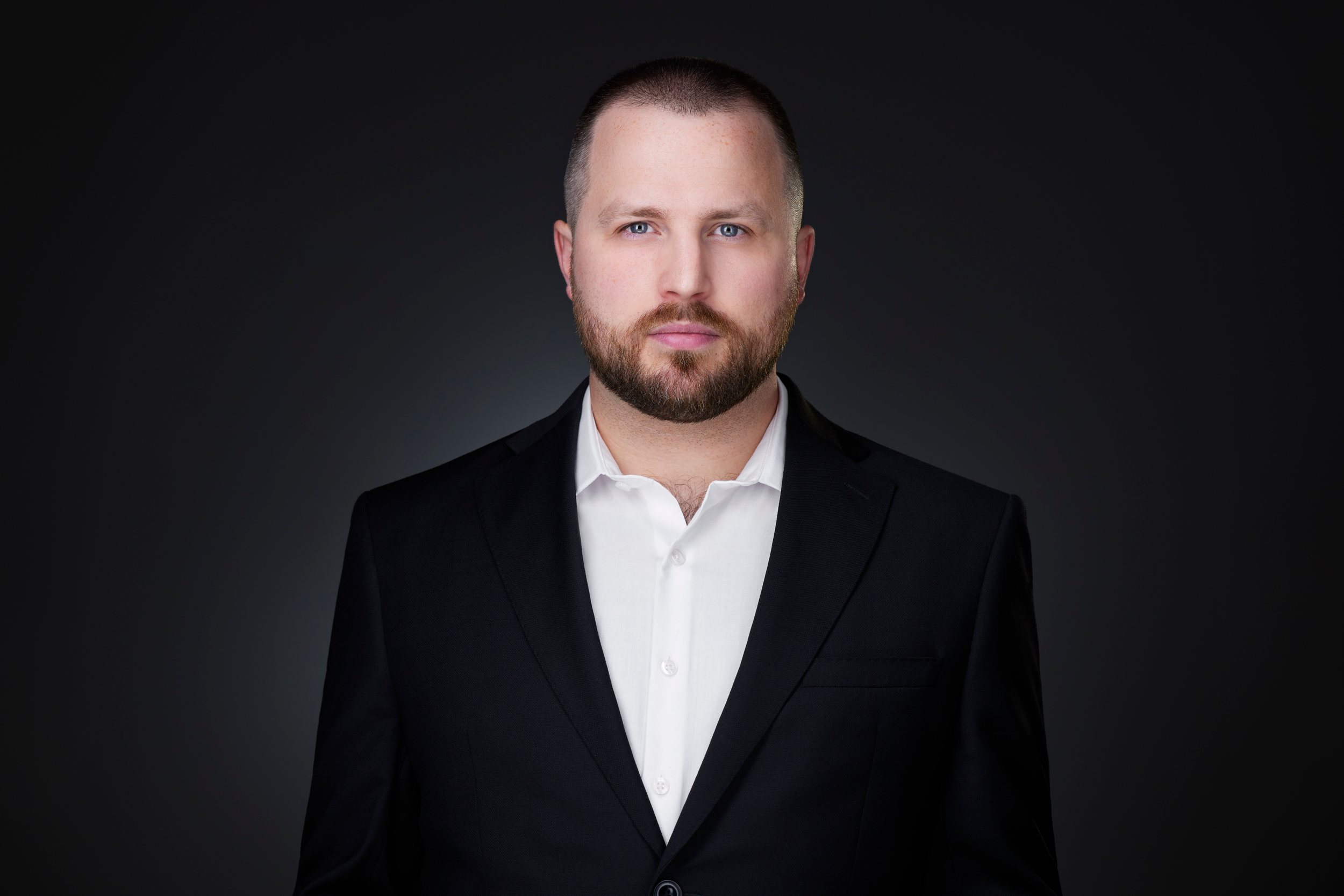 Real estate headshot: a beard, a black suit and an open white collar, on dark
