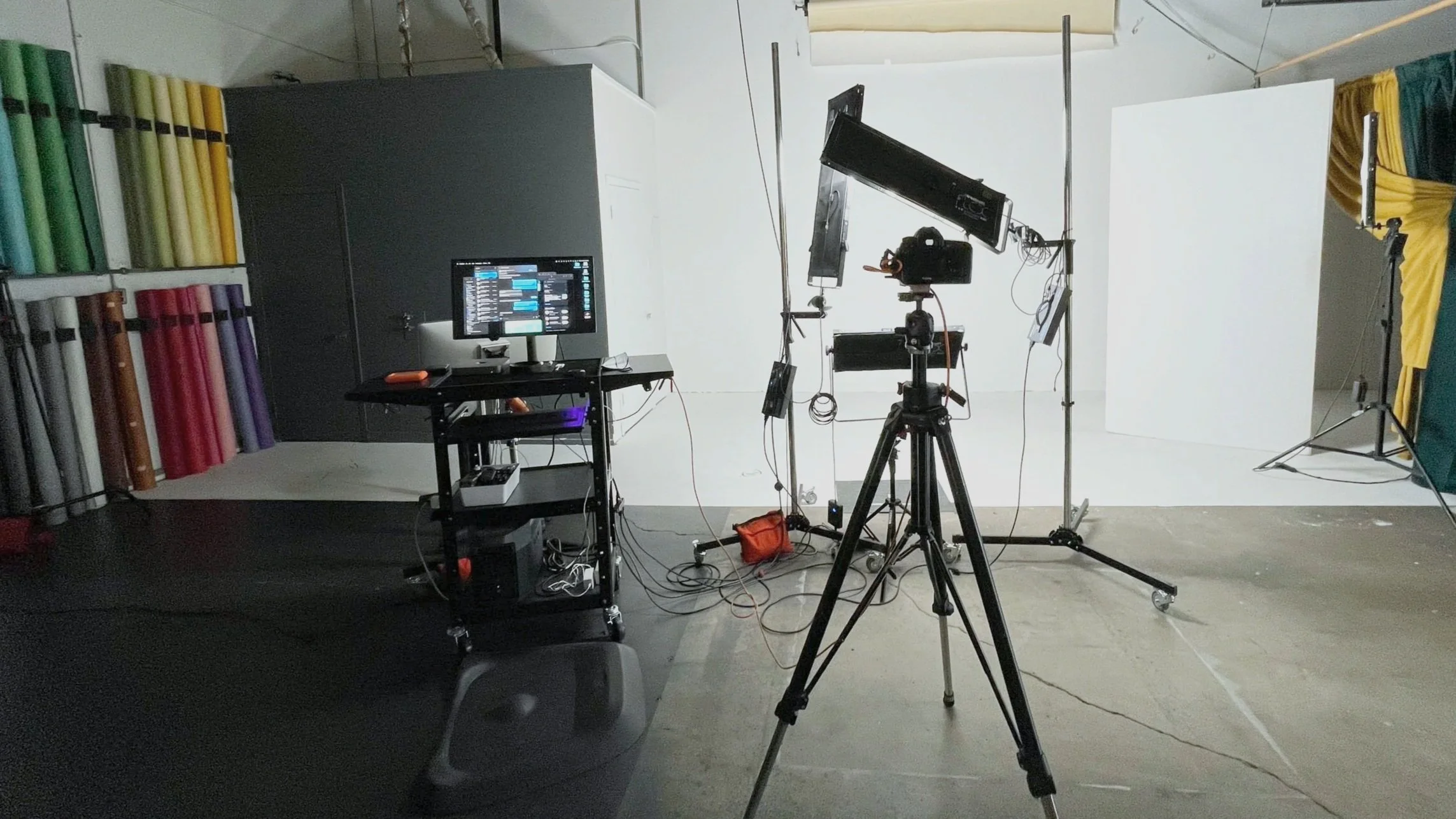 The studio set for a team day: the camera on its tripod, the tethered screen on its cart, the backdrop rolls and the white wall